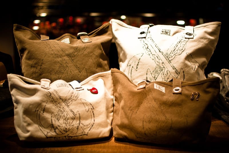 Four natural and brown canvas NEIGHBORHOOD tote bags with large illustrated graphics.
