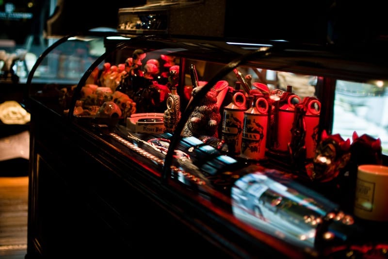 Red-lit glass case filled with NEIGHBORHOOD accessories, containers and figurines.