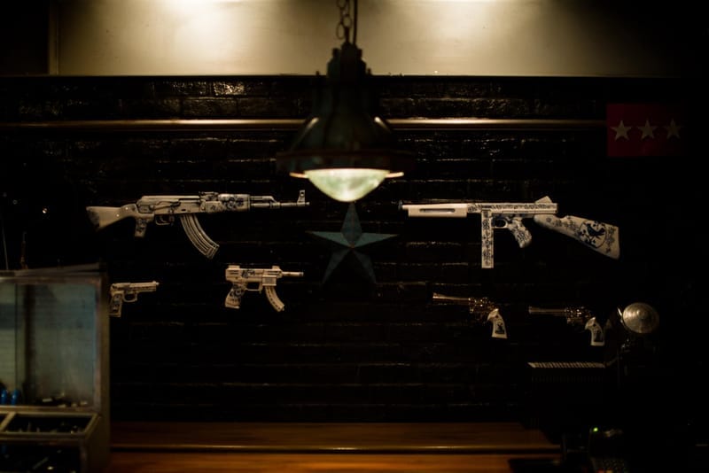 Decorated replica rifles and handguns mounted on a black brick wall at NEIGHBORHOOD Shibuya.