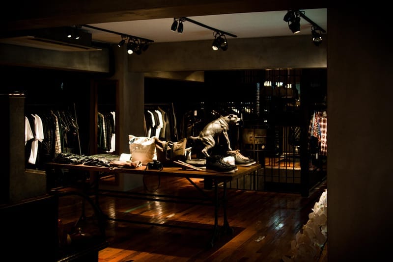 Wide view of the dim NEIGHBORHOOD Shibuya interior with display tables, clothing racks and a panther statue.