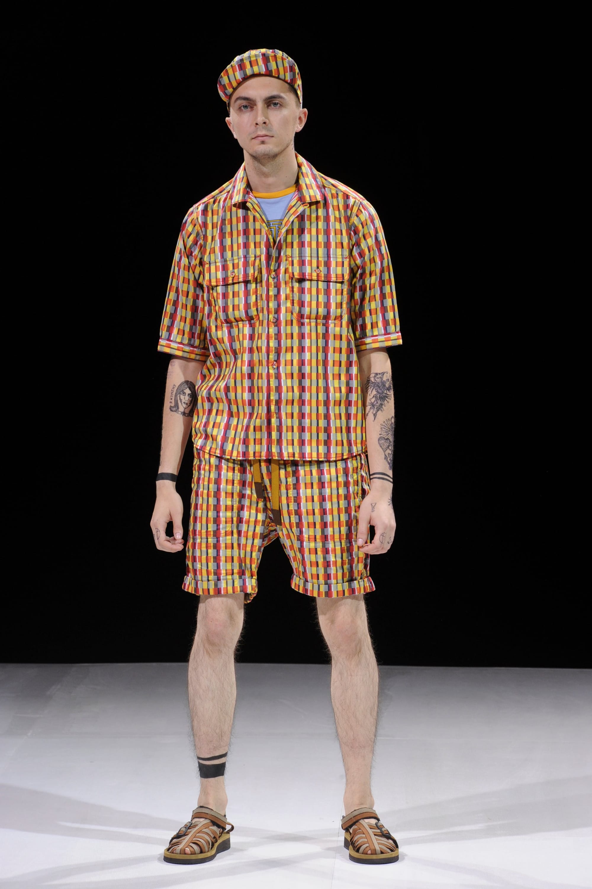 Model in a multicolor plaid short-sleeve shirt, matching shorts, and matching cap.