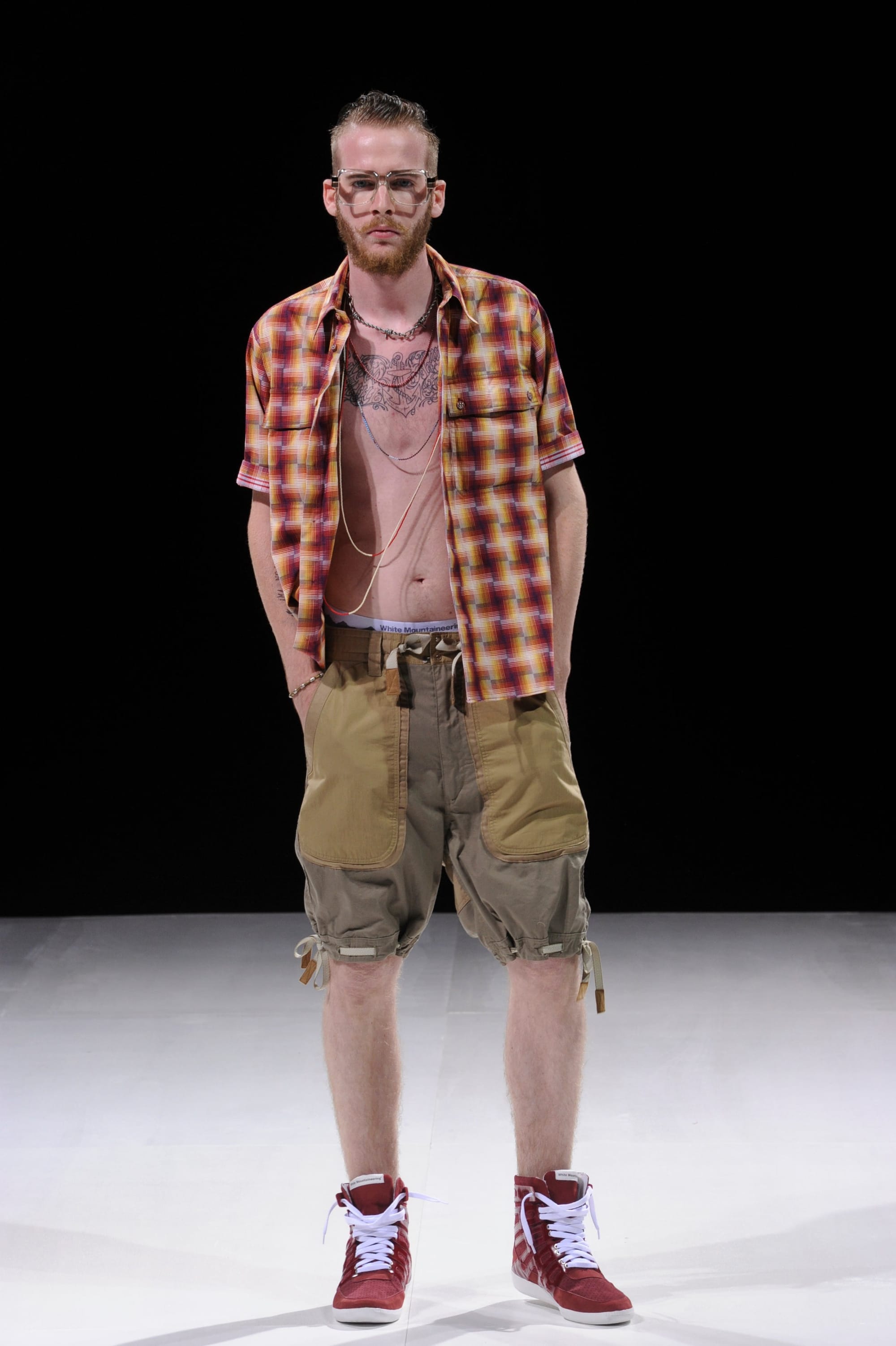 Model in an orange plaid shirt and two-tone tan and grey cargo shorts.