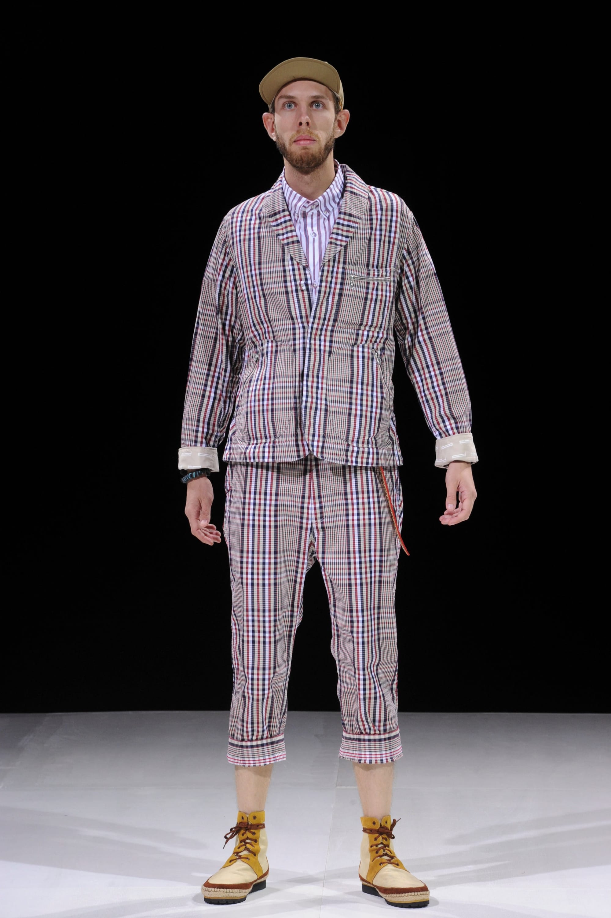 Model in a pale plaid jacket and matching cropped trousers with a tan cap.