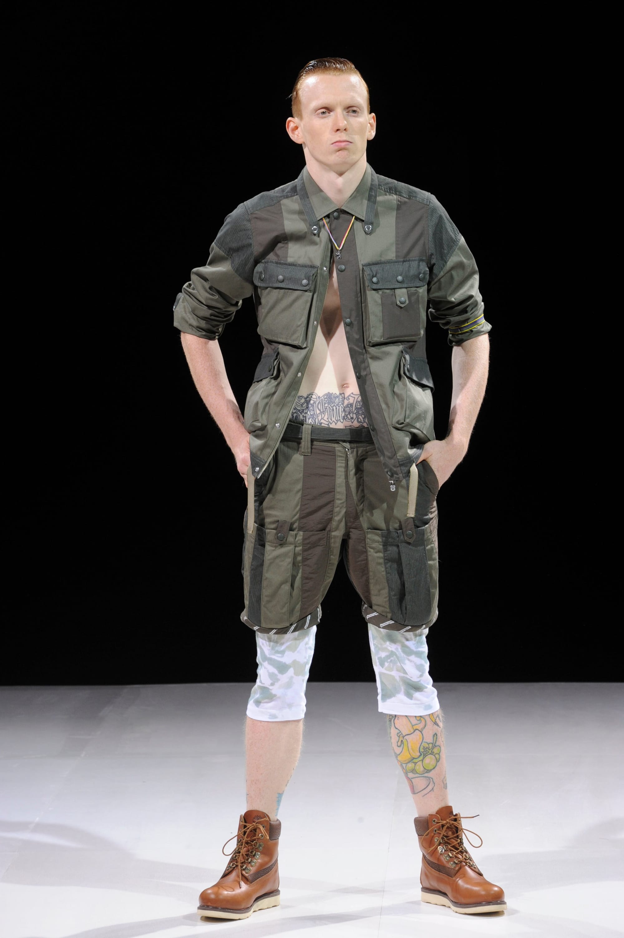 Model in an olive patchwork utility shirt and shorts layered over white printed leggings.