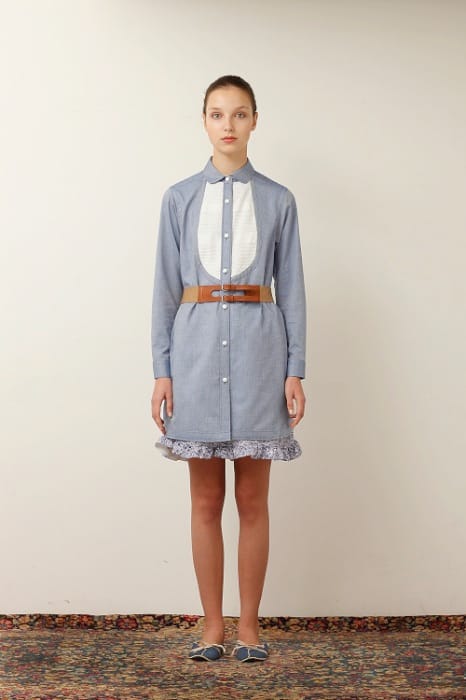 White Mountaineering womenswear model in a blue shirt dress with a white bib, double brown belt and lace-trimmed hem.
