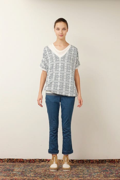 White Mountaineering womenswear model in a grey patterned V-neck top, blue jeans and tan sneakers.
