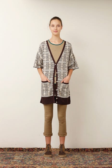 White Mountaineering womenswear model in a black-and-cream patterned long cardigan, brown top and tan cropped trousers.