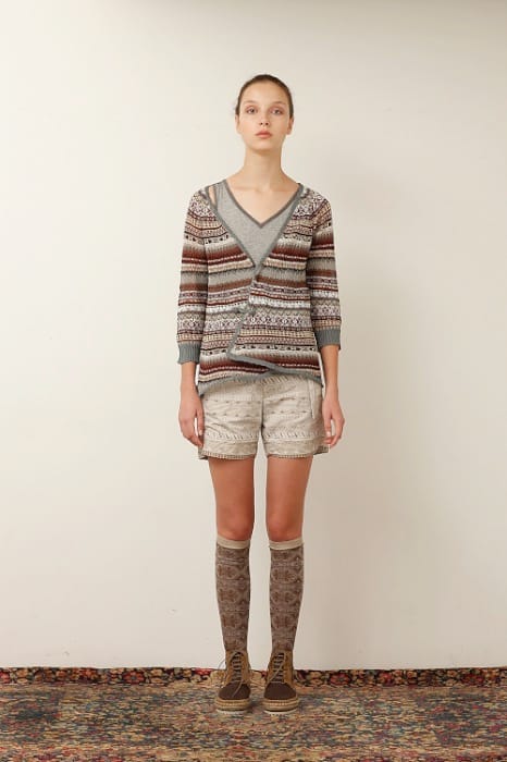 White Mountaineering womenswear model in a patterned cardigan, embroidered cream shorts, patterned knee socks and brown boots.