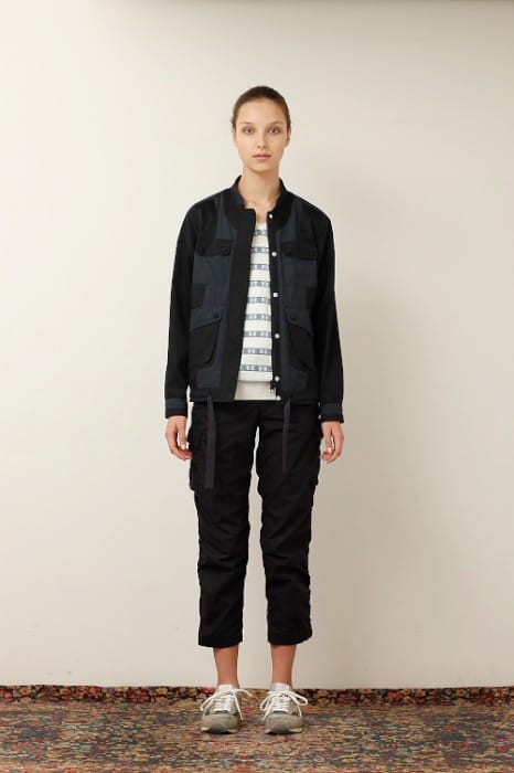White Mountaineering womenswear model in a black field jacket, striped top and black cropped cargo trousers.