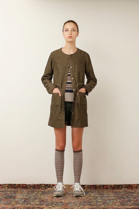 White Mountaineering womenswear model in a brown collarless long coat, striped top, black shorts and patterned knee socks.