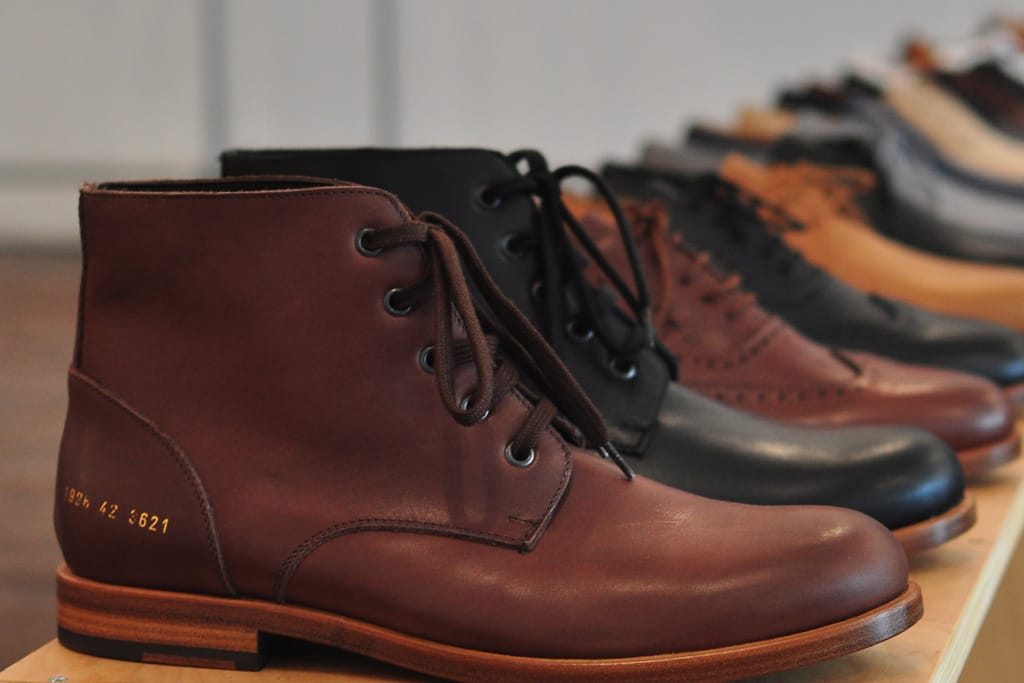 Brown and black Common Projects ankle boots and brogues arranged in a showroom lineup.