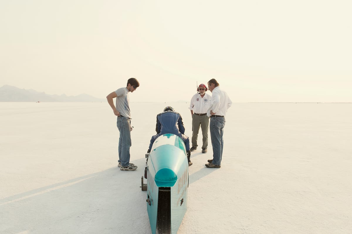 Rider seated in a turquoise streamliner motorcycle as the course starter and crew look on at Bonneville SpeedWeek 2012.