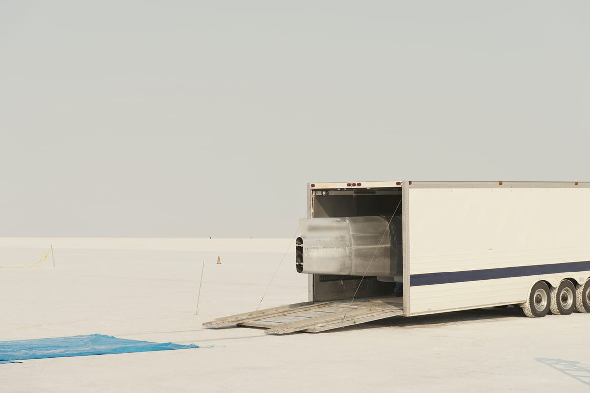 Rear of a silver streamliner protruding from an open transport trailer on the Bonneville Salt Flats.