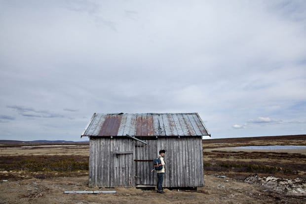 Sandqvist Fall/Winter 2011: Person with blue backpack stands beside a weathered wooden hut.