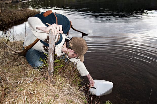 Sandqvist Fall/Winter 2011: Person wearing a blue backpack fills a white container beside a lake.