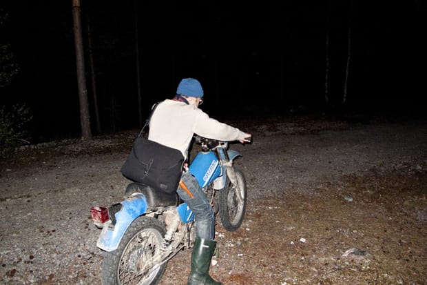 Sandqvist Fall/Winter 2011: Person with black messenger bag rides a blue motorcycle on a forest road.