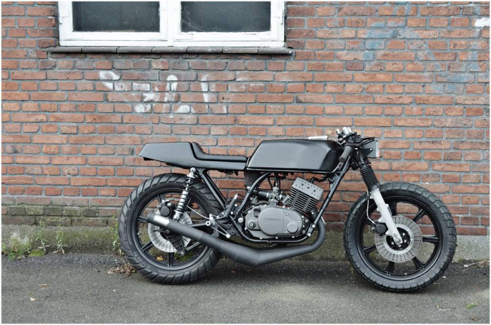 Right-side profile of the black Wrenchmonkees Yamaha RD400 café racer against a brick wall.