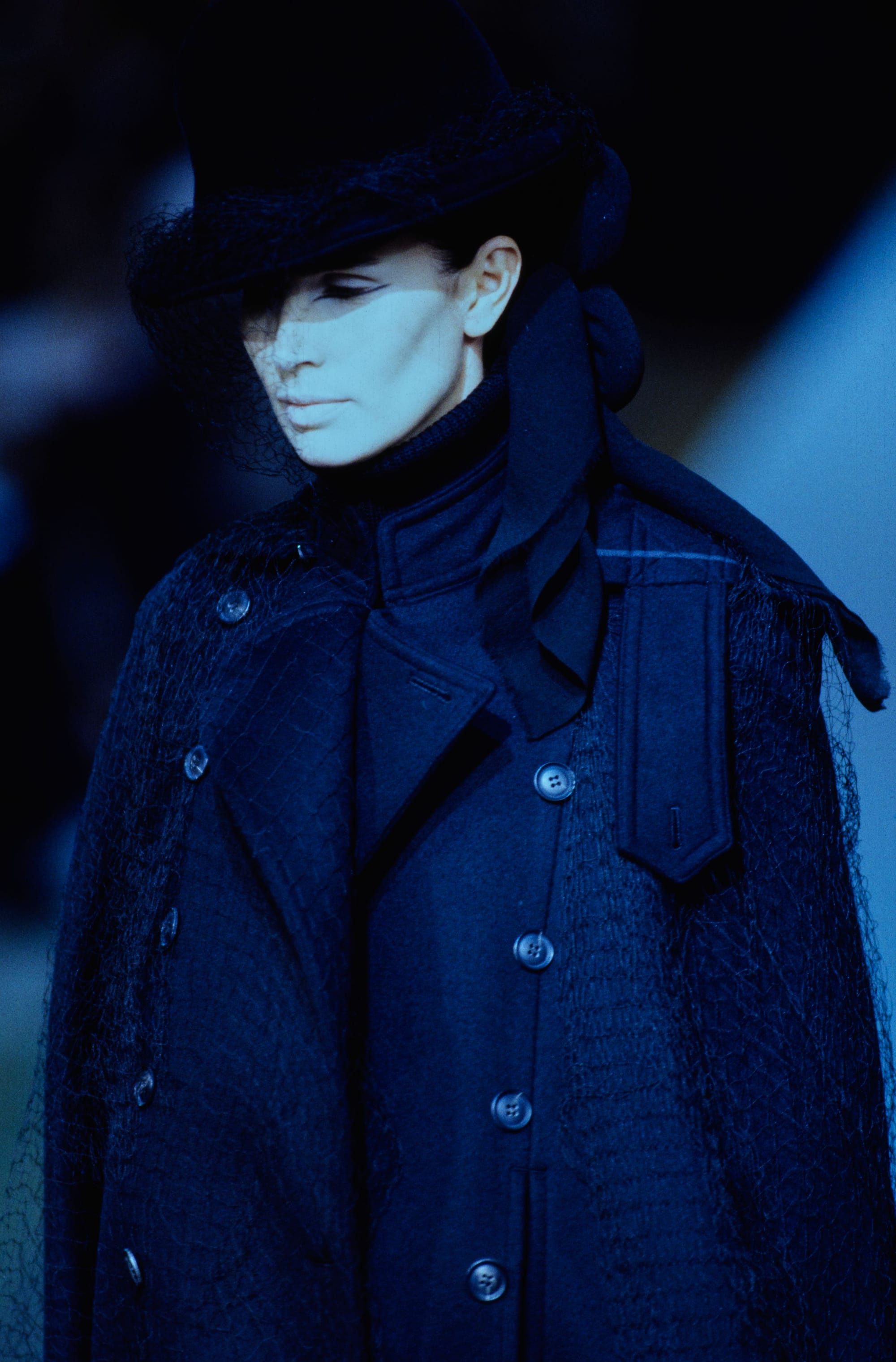 Yohji Yamamoto Fall 1995 detail 1: Black veiled hat above a layered navy coat with netted shoulder fabric.