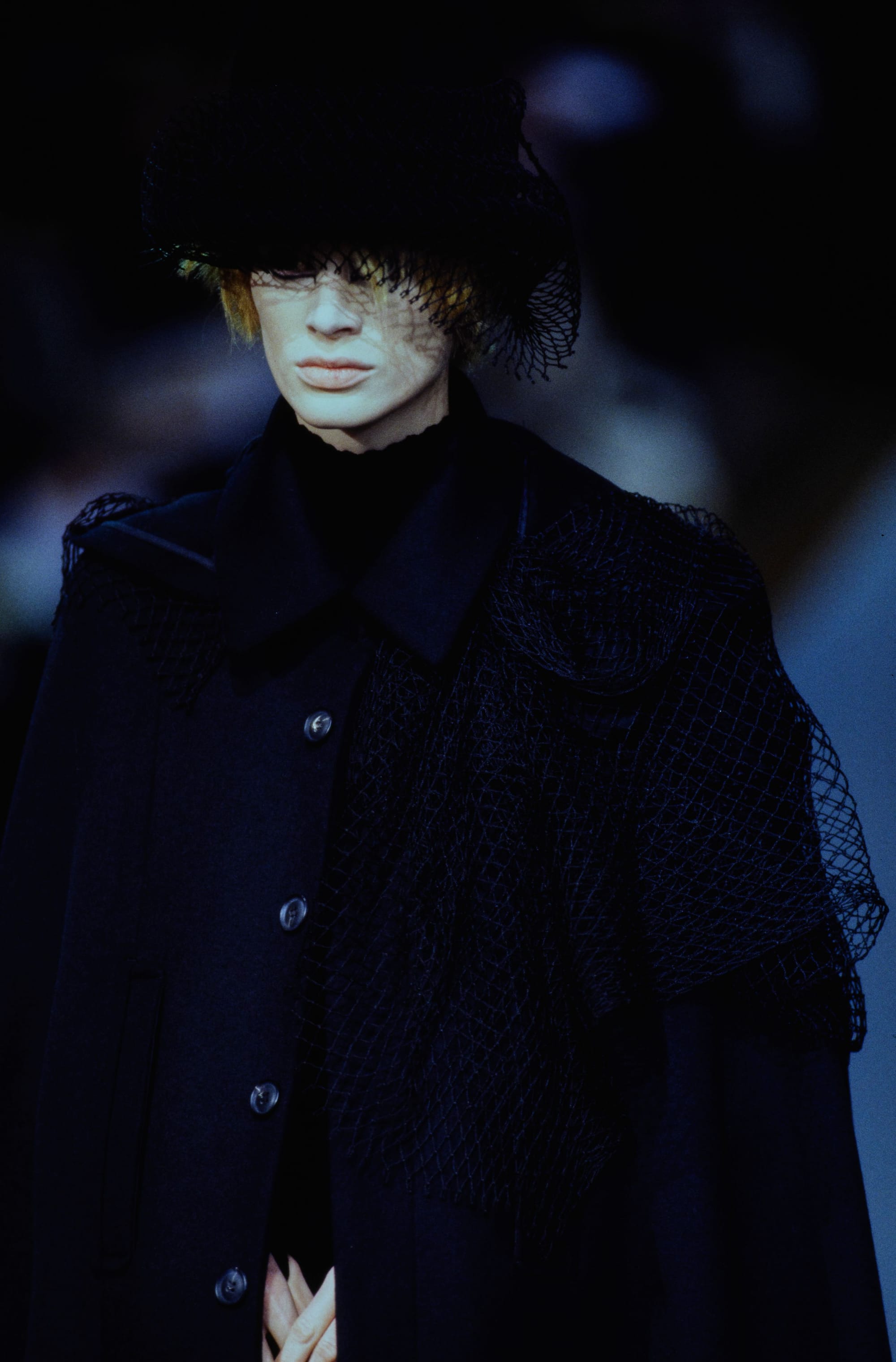 Yohji Yamamoto Fall 1995 detail 2: Brimmed hat with a black mesh veil over a buttoned navy coat and draped netting.
