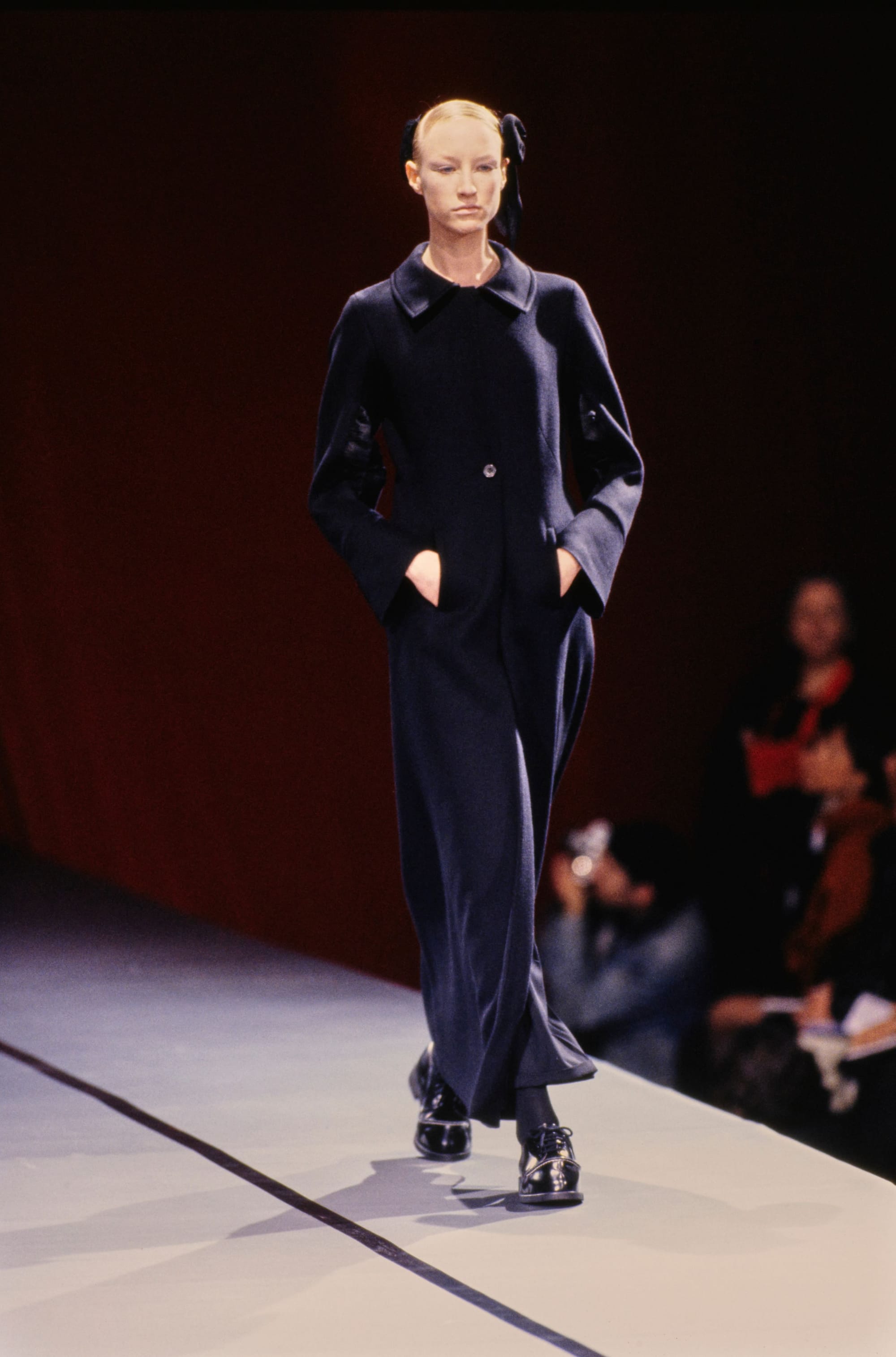 Yohji Yamamoto Fall 1995 detail 8: Floor-length dark button-front coat with hands in pockets and black lace-up shoes.