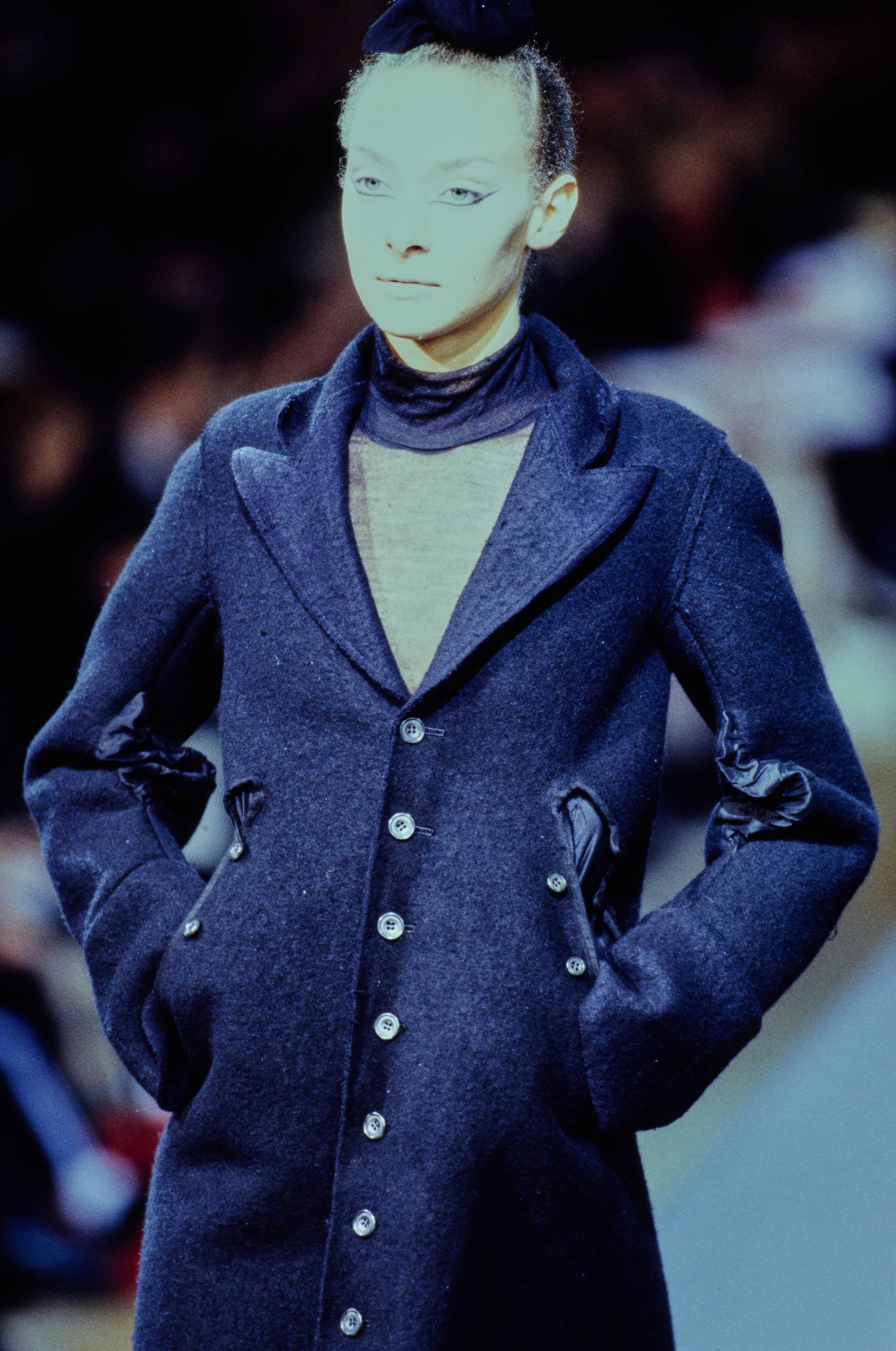 Yohji Yamamoto Fall 1995 detail 10: Close view of a fitted navy coat with angled buttoned pockets and a sheer neckline.