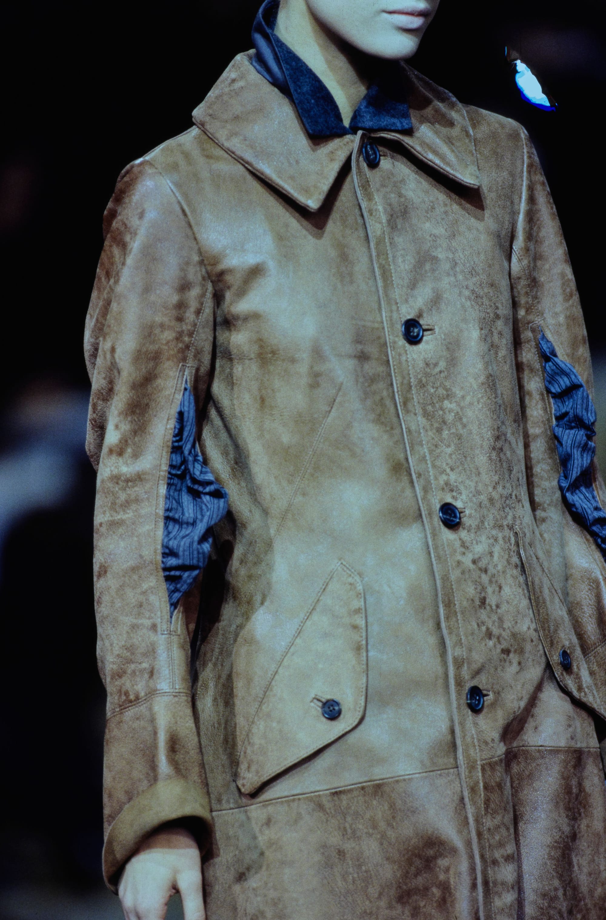 Yohji Yamamoto Fall 1995 detail 13: Tan mottled coat with a broad collar, dark buttons and blue striped fabric at the sleeves.