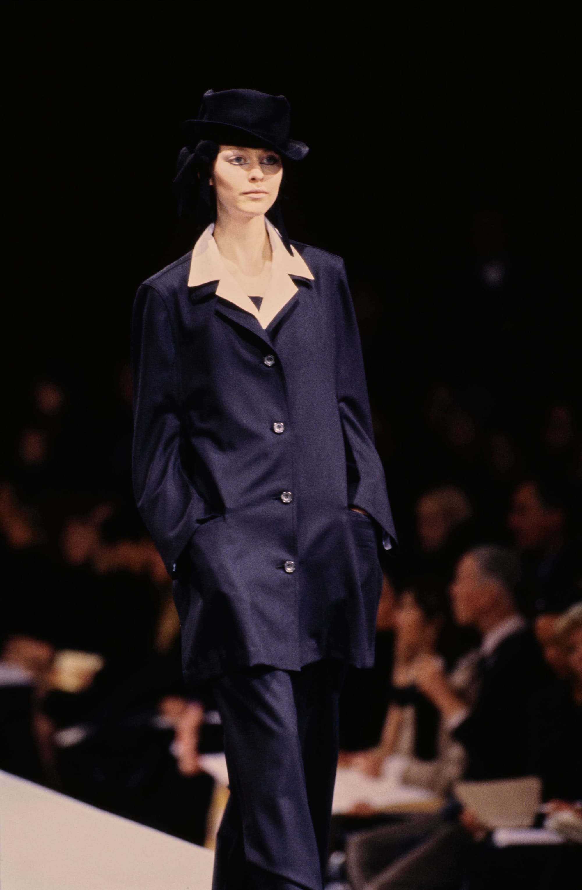Yohji Yamamoto Fall 1995 detail 17: Dark tailored jacket and trousers with a pale collar and black hat.
