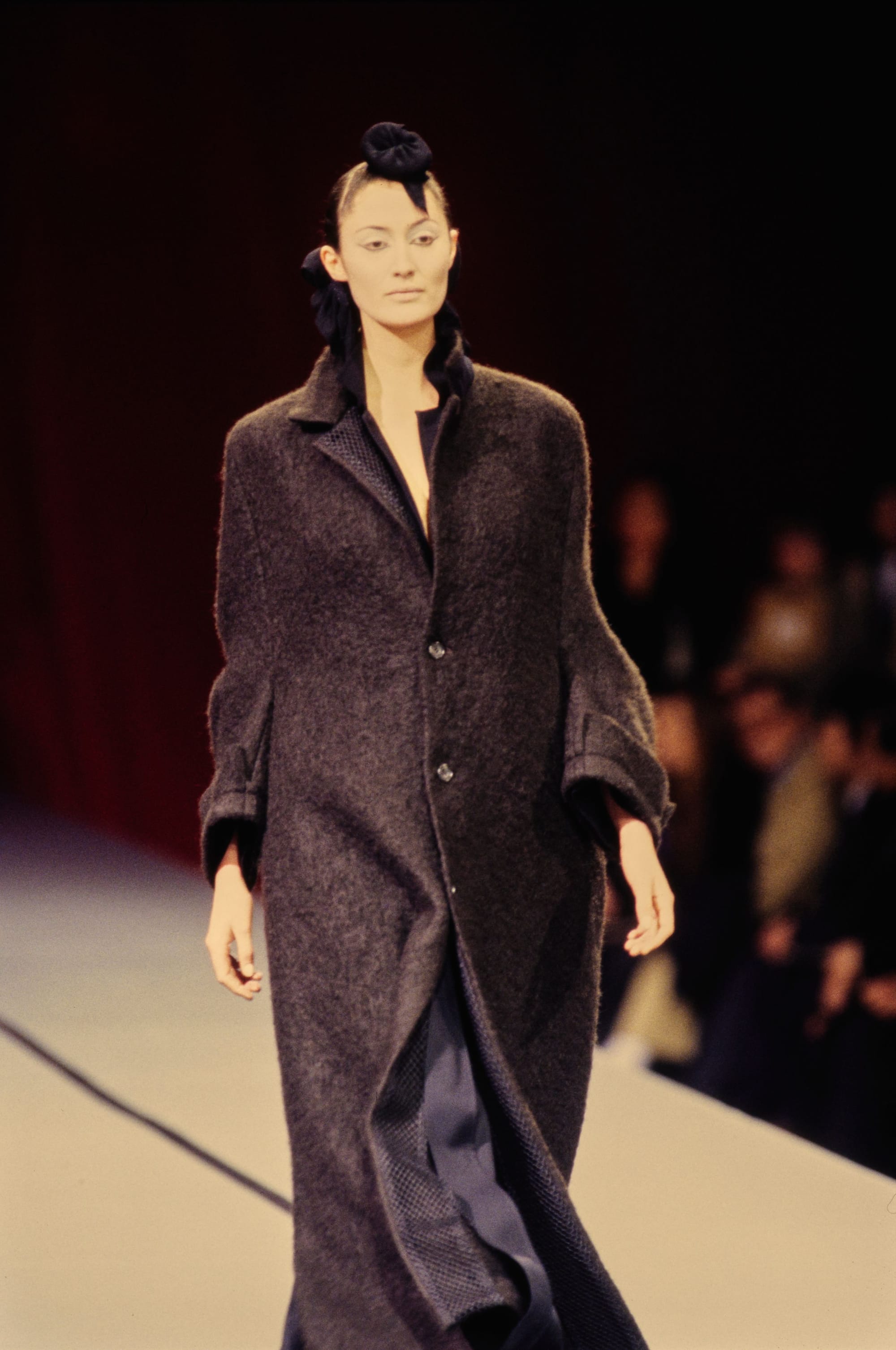 Yohji Yamamoto Fall 1995 detail 18: Long charcoal textured coat with broad sleeves and a black hair ornament.