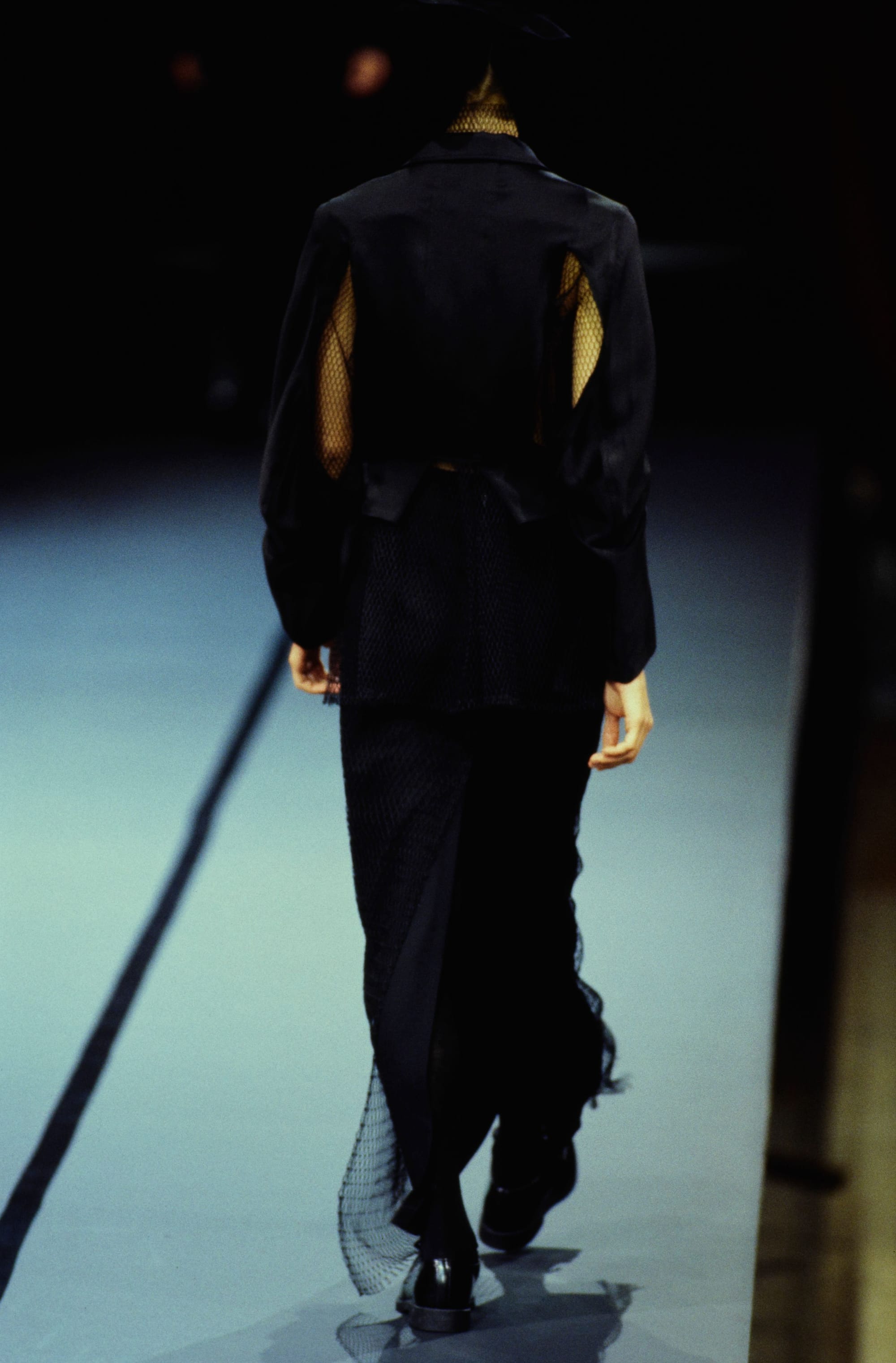 Yohji Yamamoto Fall 1995 detail 21: Rear black jacket with mesh openings at the sleeves and netting trailing below the skirt.