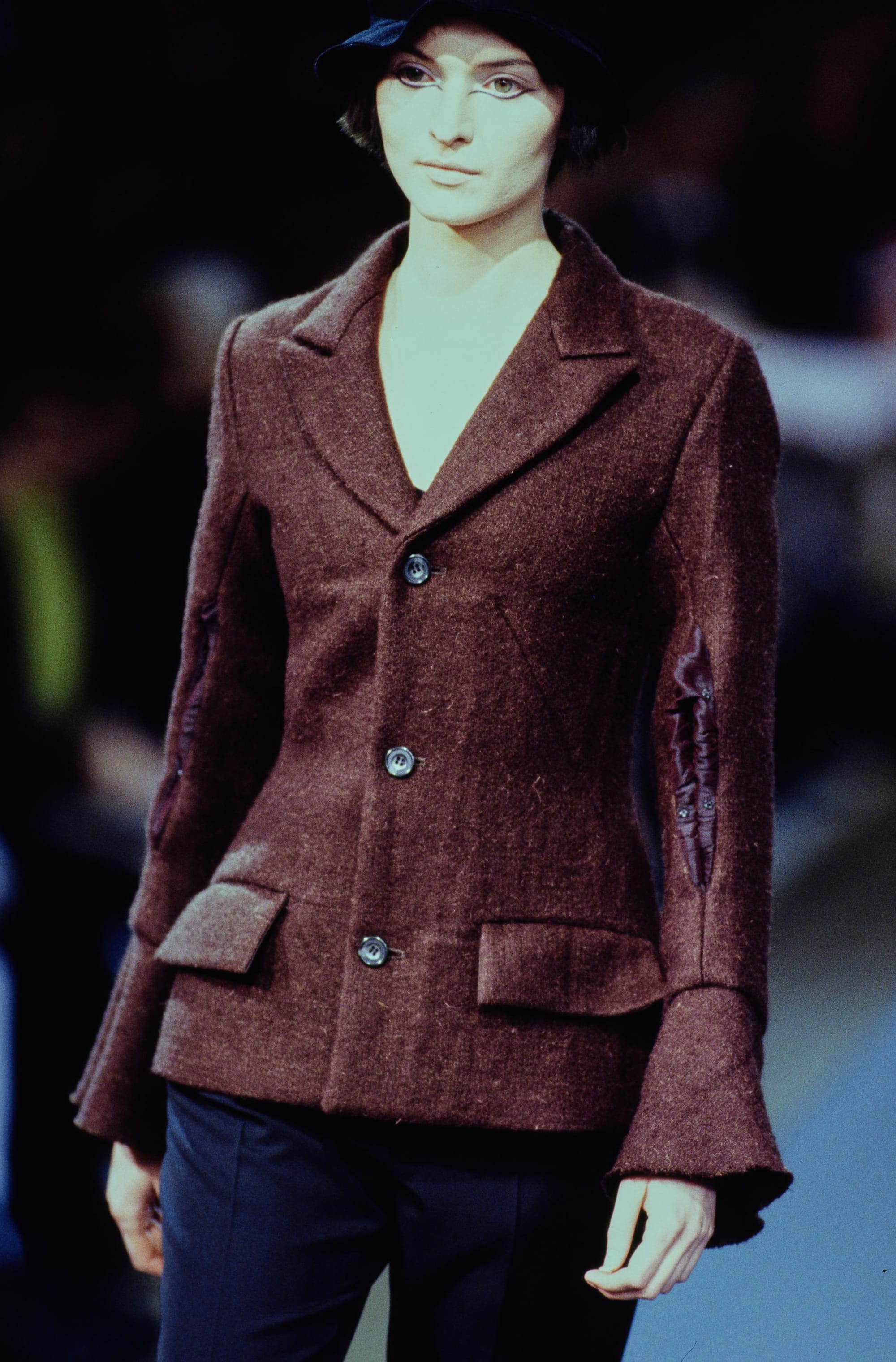 Yohji Yamamoto Fall 1995 detail 25: Burgundy fitted jacket with flared cuffs and flap pockets over dark trousers.