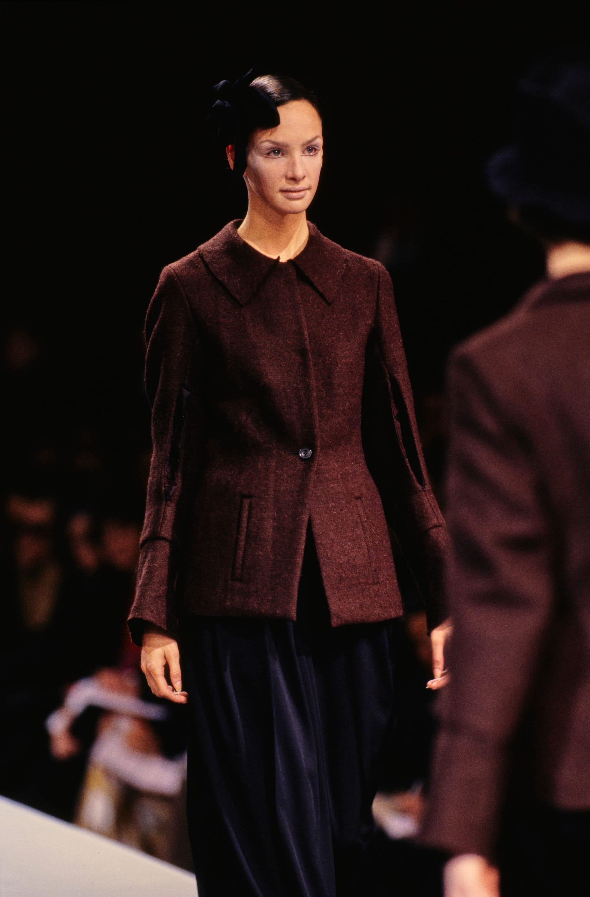Yohji Yamamoto Fall 1995 detail 26: Burgundy buttoned jacket with a pointed collar over a dark draped lower garment.