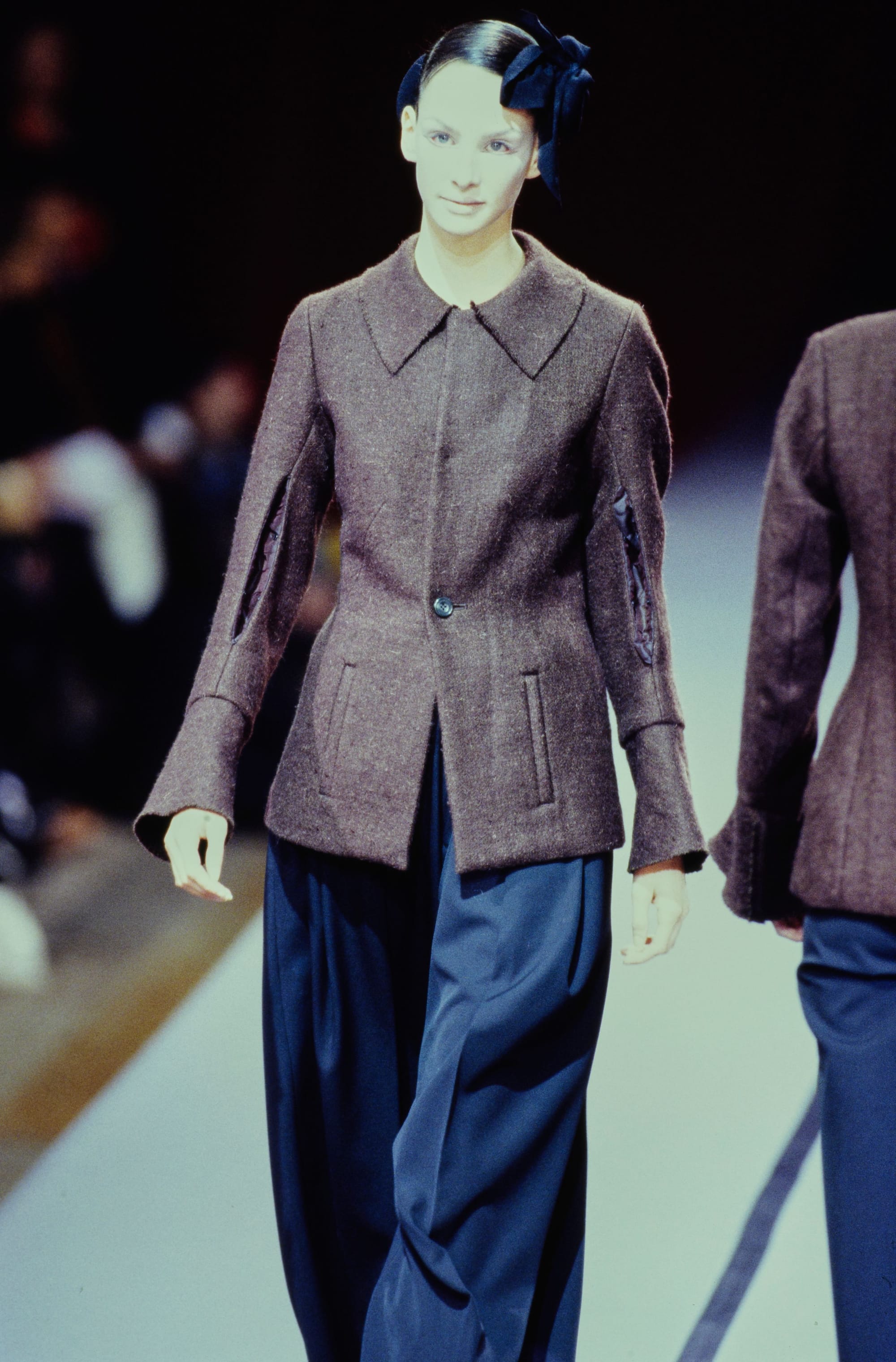 Yohji Yamamoto Fall 1995 detail 27: Grey fitted jacket with long cuffs and vertical pockets above wide navy trousers.