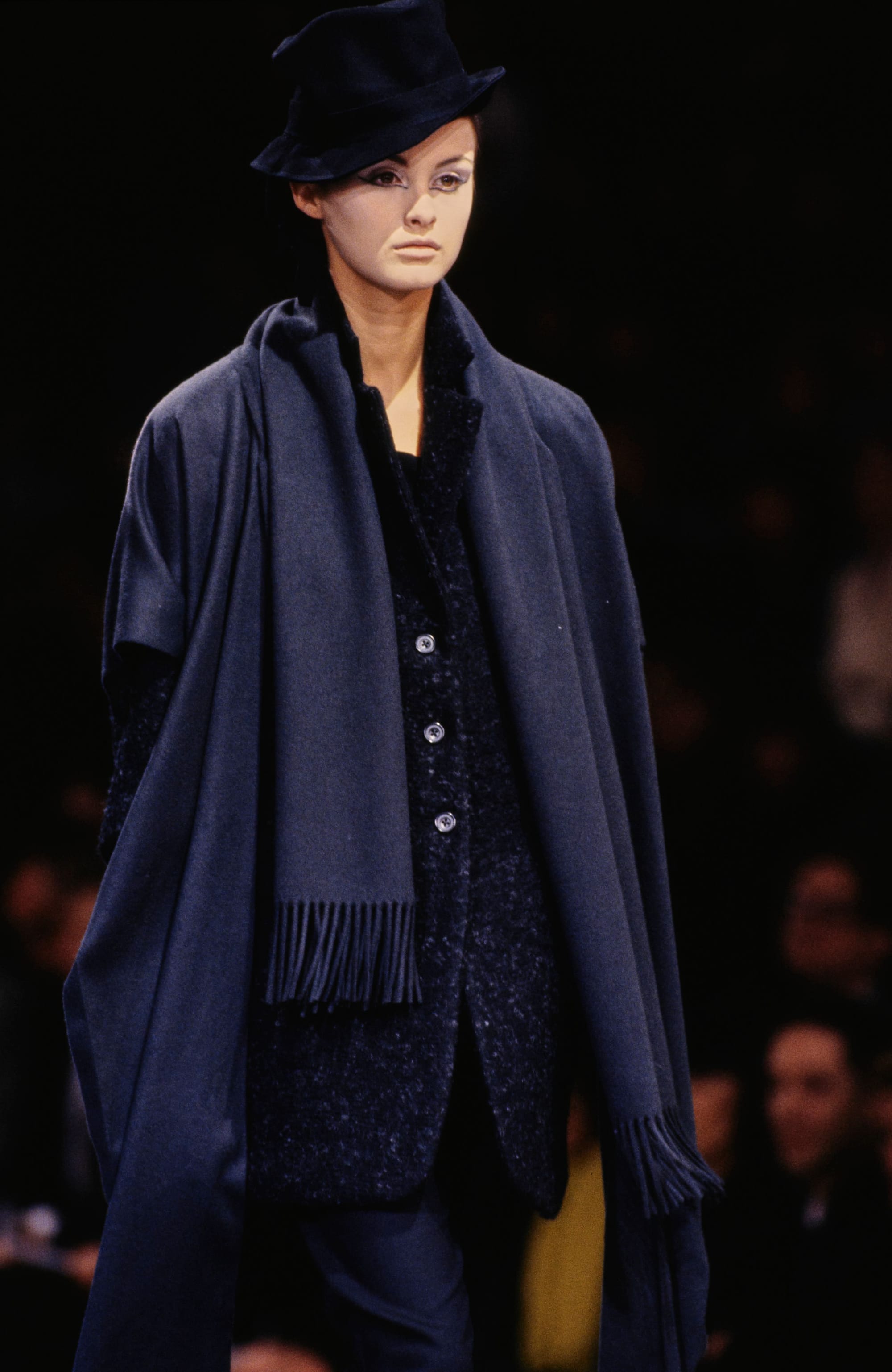 Yohji Yamamoto Fall 1995 detail 29: Black hat above a dark textured jacket and a long navy fringed scarf.