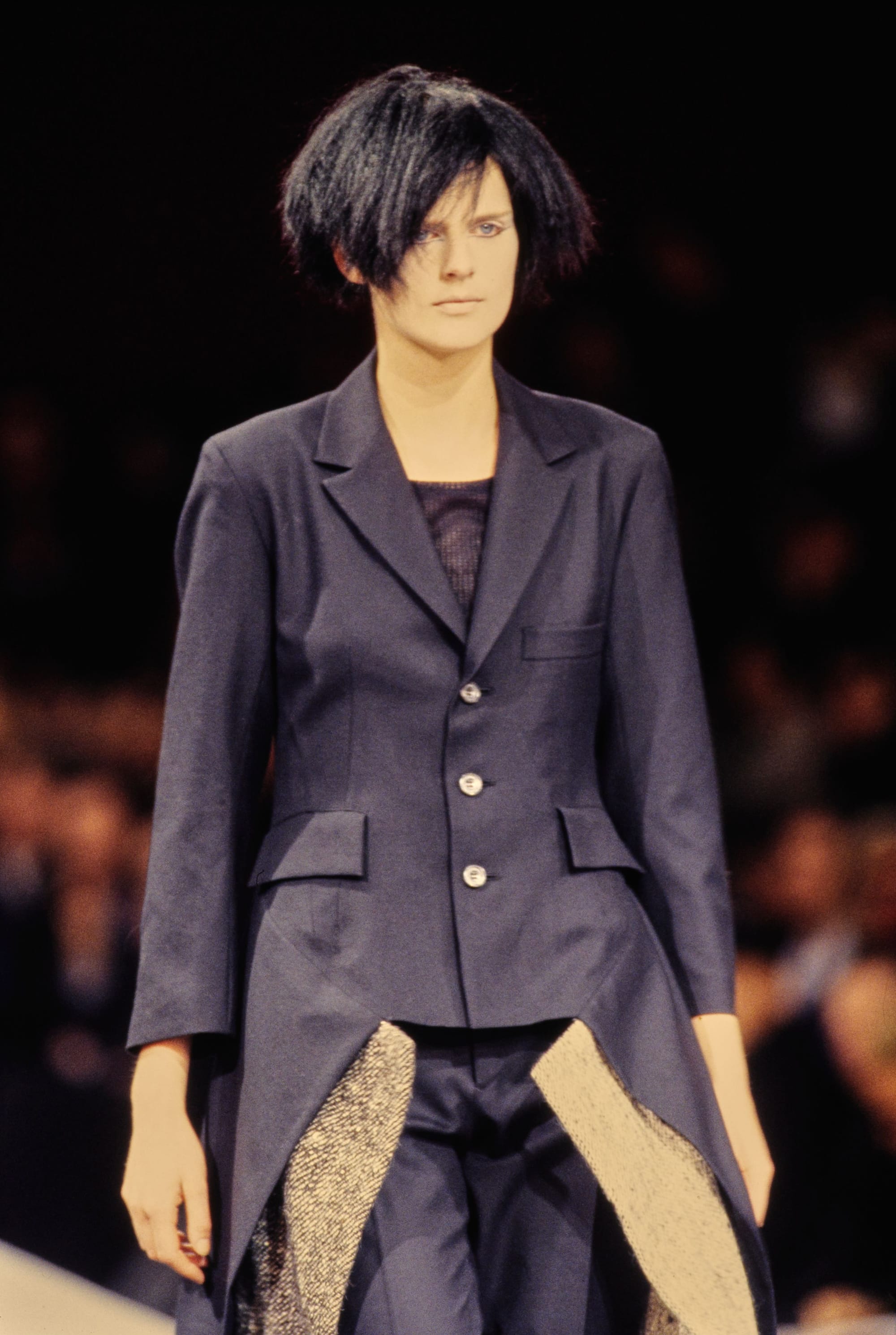 Yohji Yamamoto Fall 1995 detail 30: Navy tailored jacket with pointed front tails exposing beige net panels below.