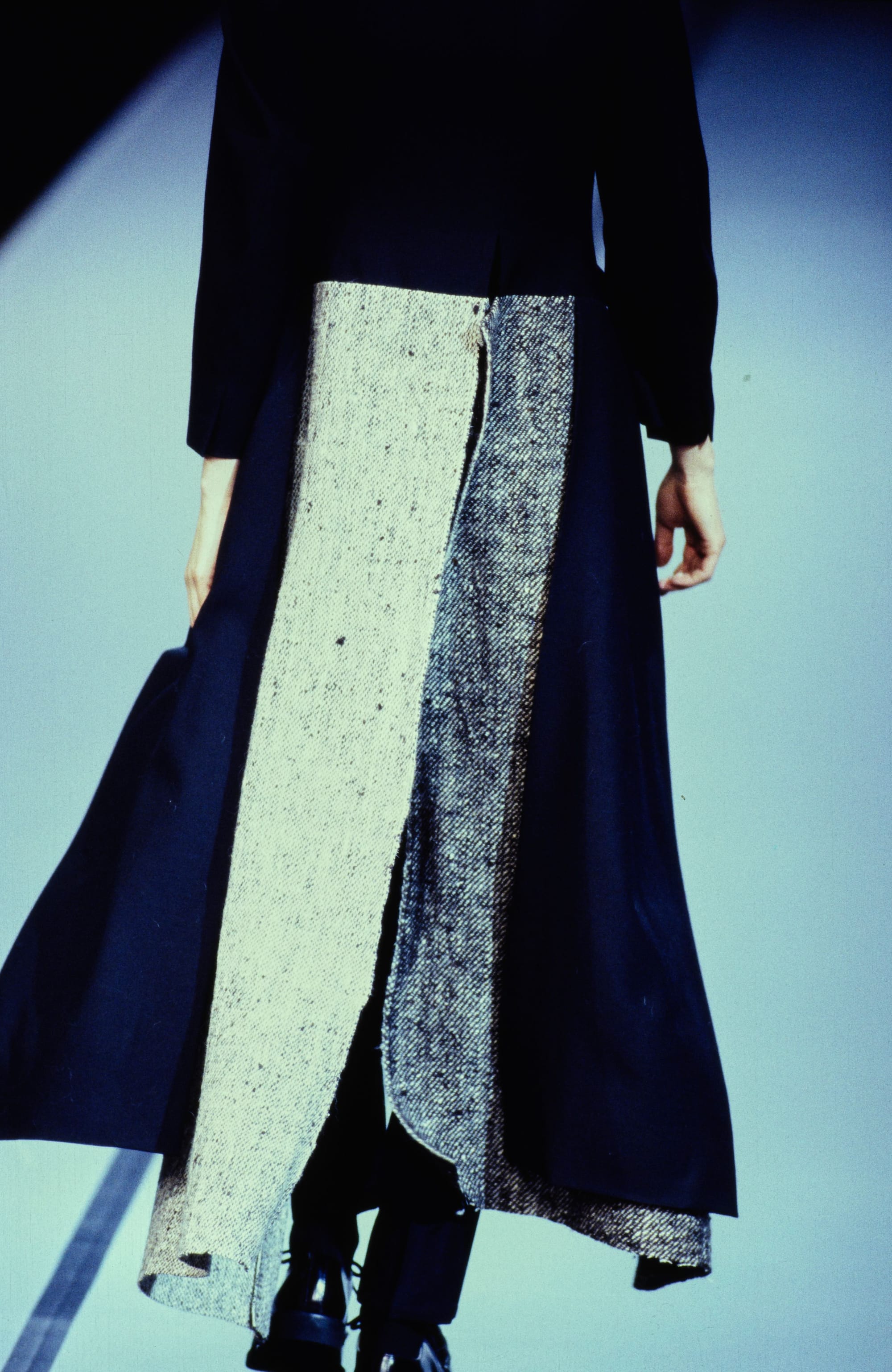 Yohji Yamamoto Fall 1995 detail 31: Rear detail of a dark skirt with two long cream textured panels hanging at the center.