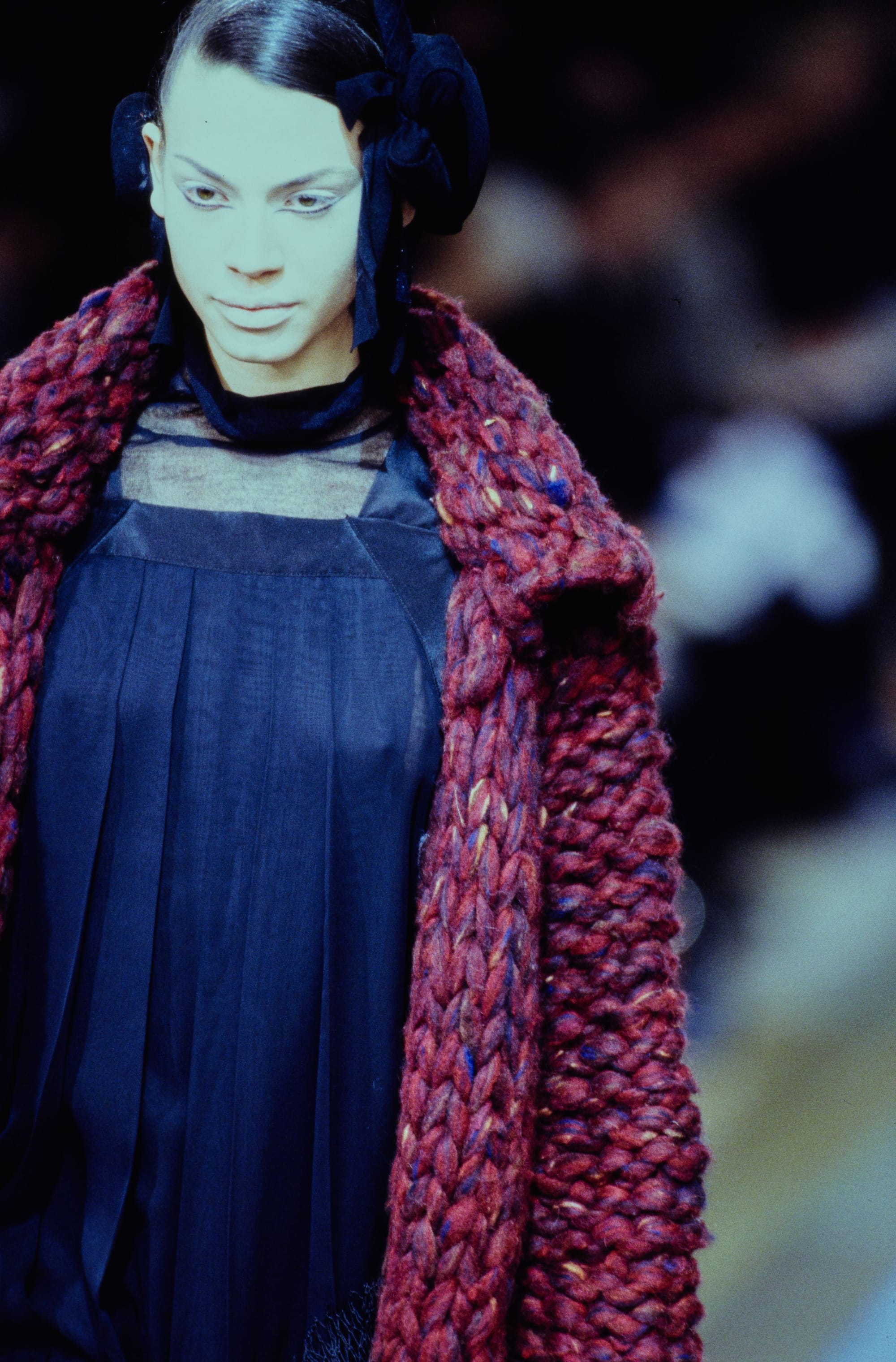 Yohji Yamamoto Fall 1995 detail 33: Berry-red chunky knit coat over a navy pleated dress with a sheer neckline.
