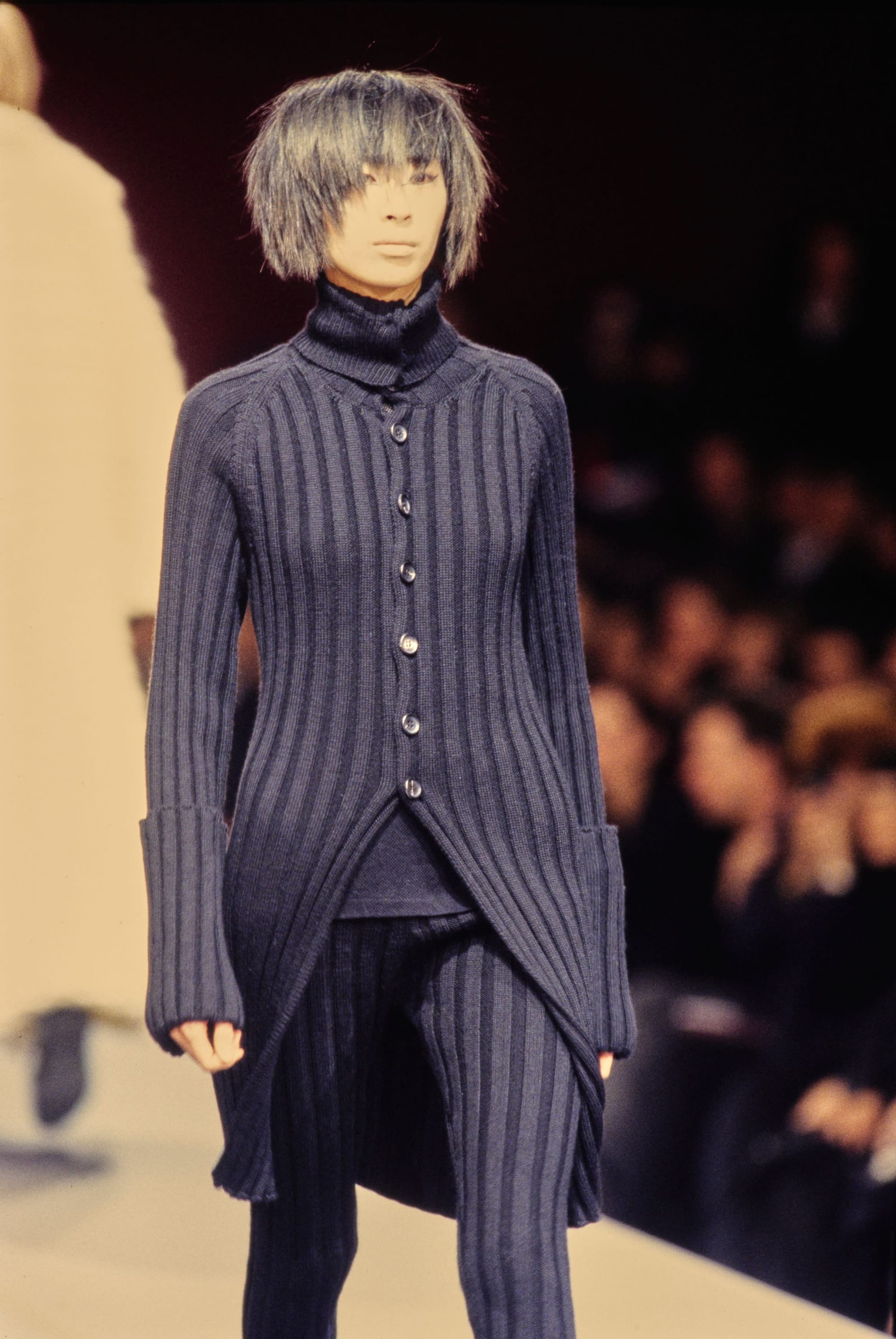 Yohji Yamamoto Fall 1995 detail 37: Ribbed dark navy cardigan with a pointed asymmetric hem and matching striped trousers.