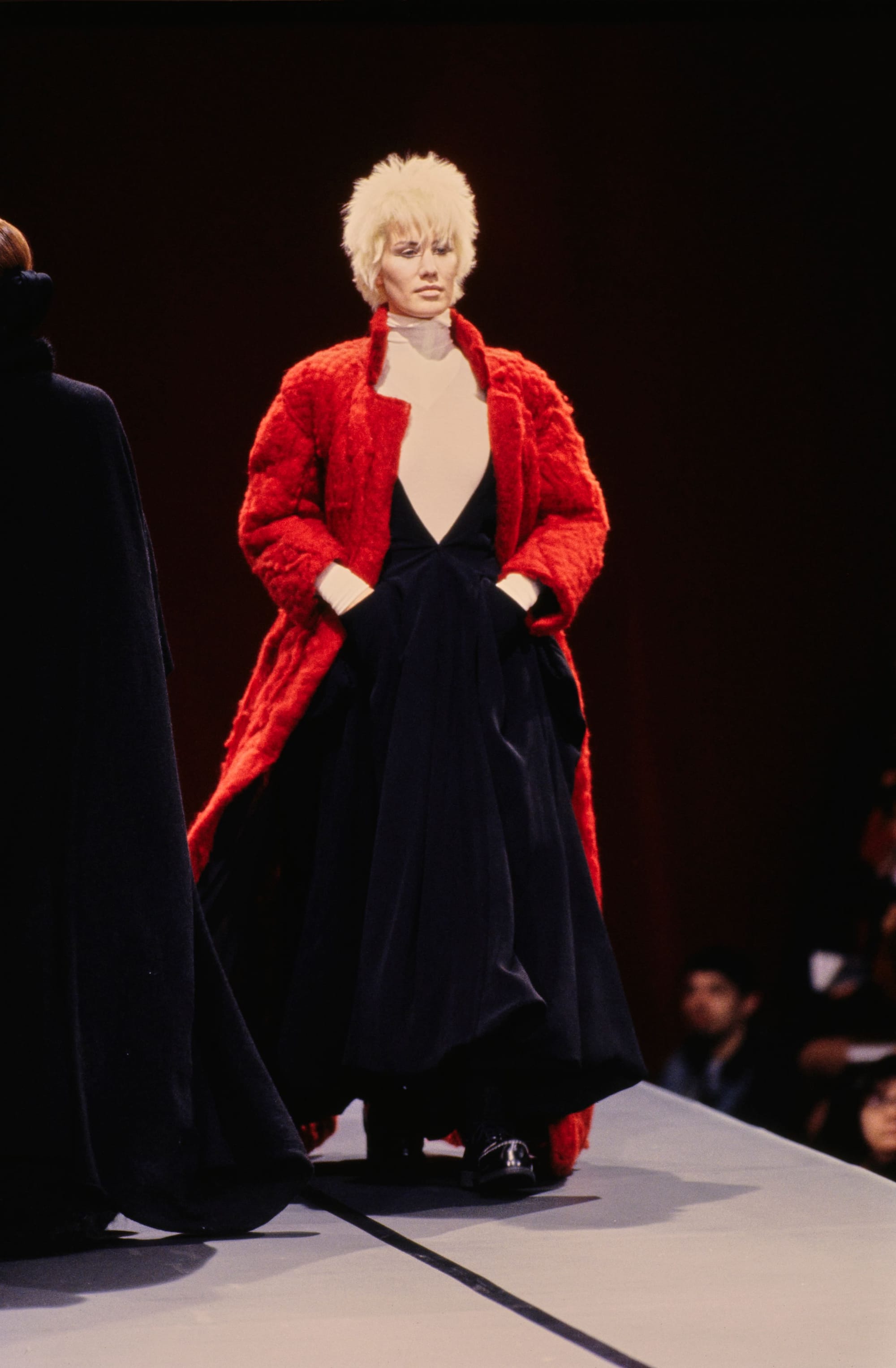 Yohji Yamamoto Fall 1995 detail 40: Bright red textured long coat over a full black dress with a sheer V-shaped front.