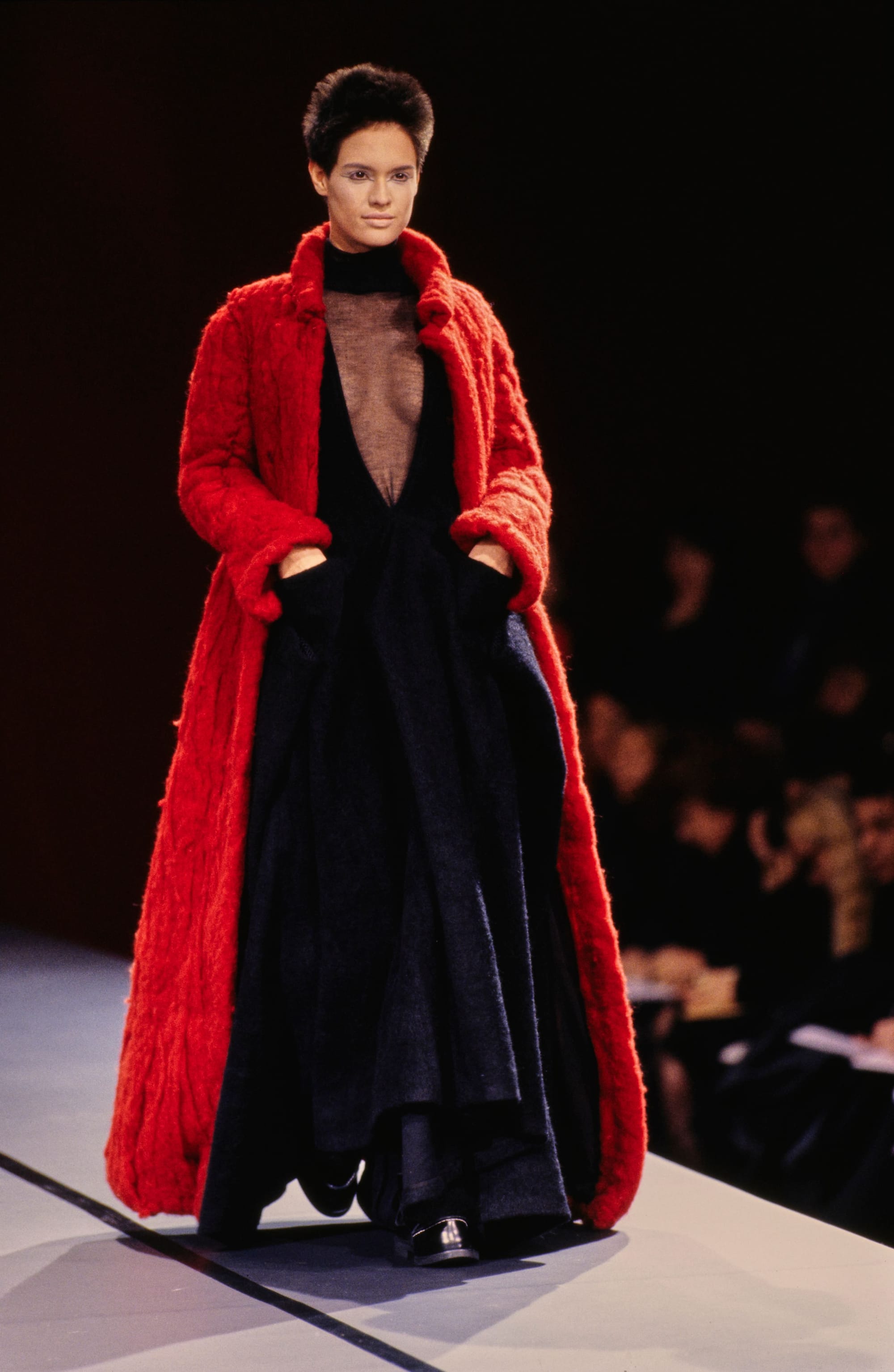 Yohji Yamamoto Fall 1995 detail 41: Bright red long coat framing a voluminous black dress, with both hands in pockets.