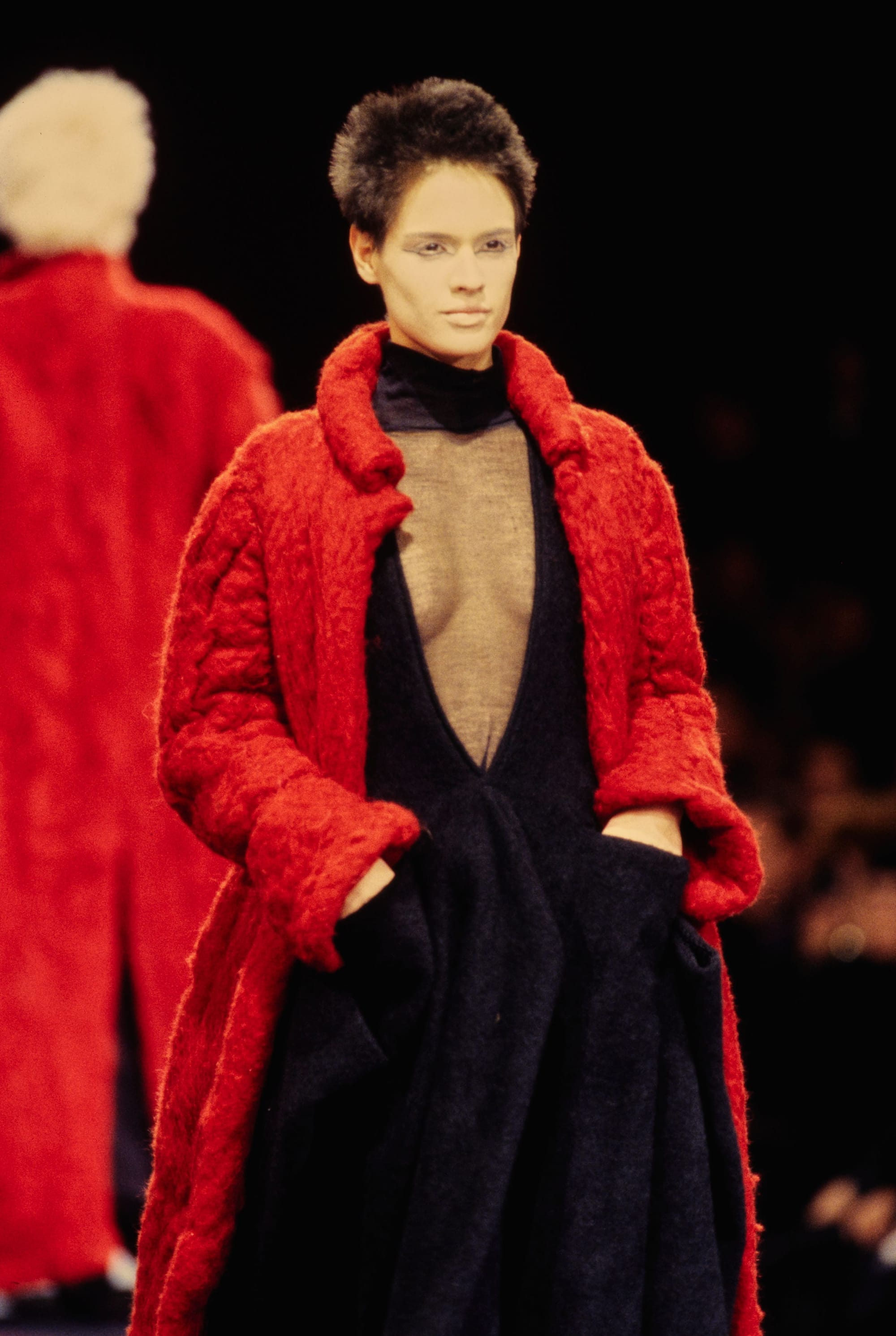 Yohji Yamamoto Fall 1995 detail 42: Closer view of a red textured coat over a black deep-V dress and sheer chest panel.