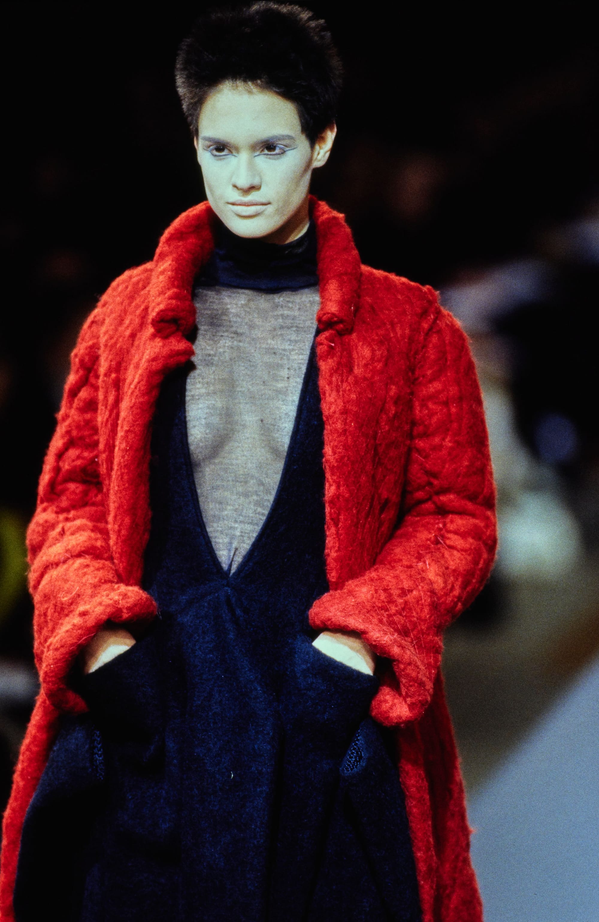 Yohji Yamamoto Fall 1995 detail 43: Portrait of a model in a bright red textured coat over a deep-V black dress.