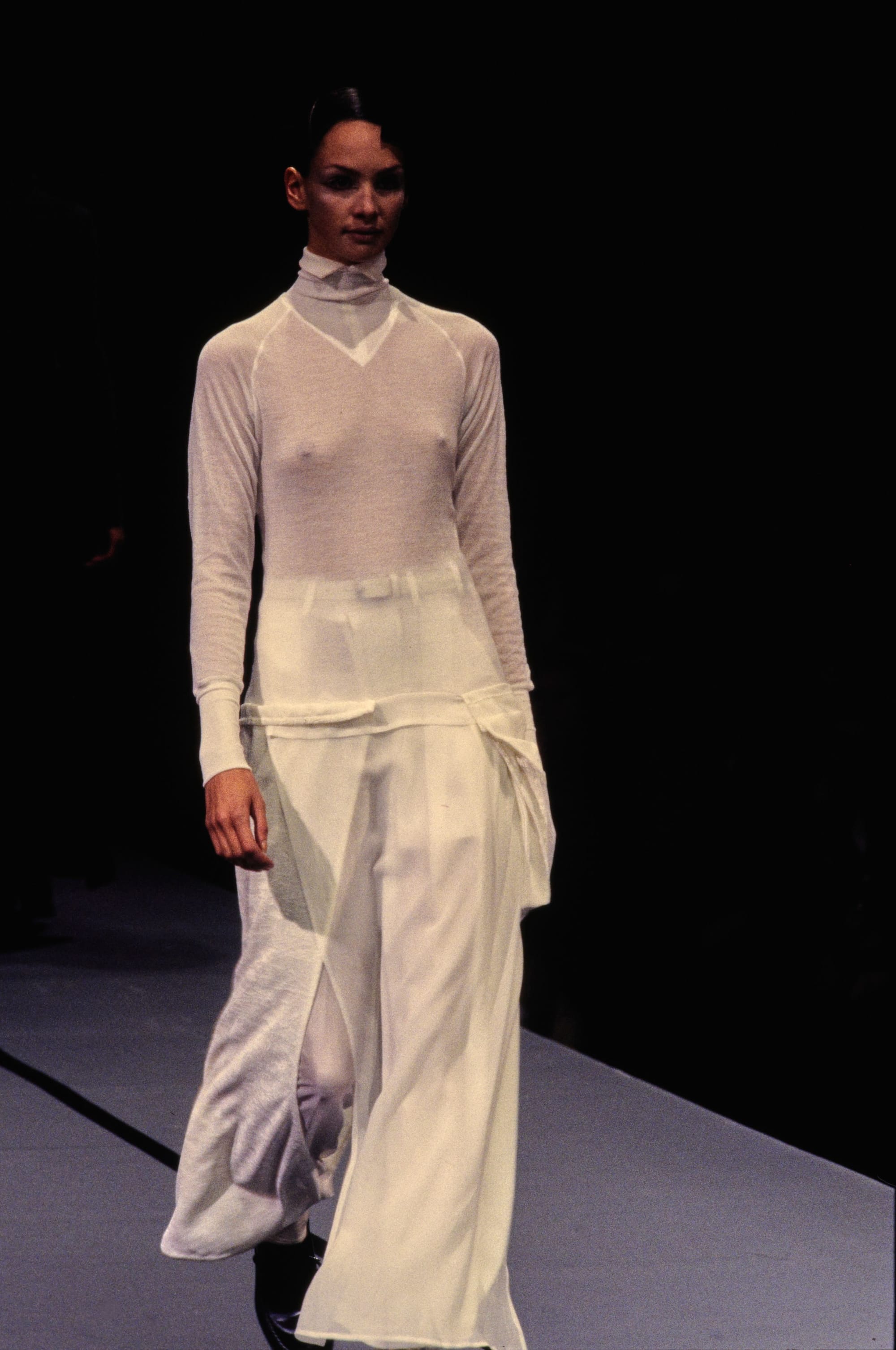 Yohji Yamamoto Fall 1995 detail 46: White high-neck lightweight top with long sleeves above loose white draped bottoms.