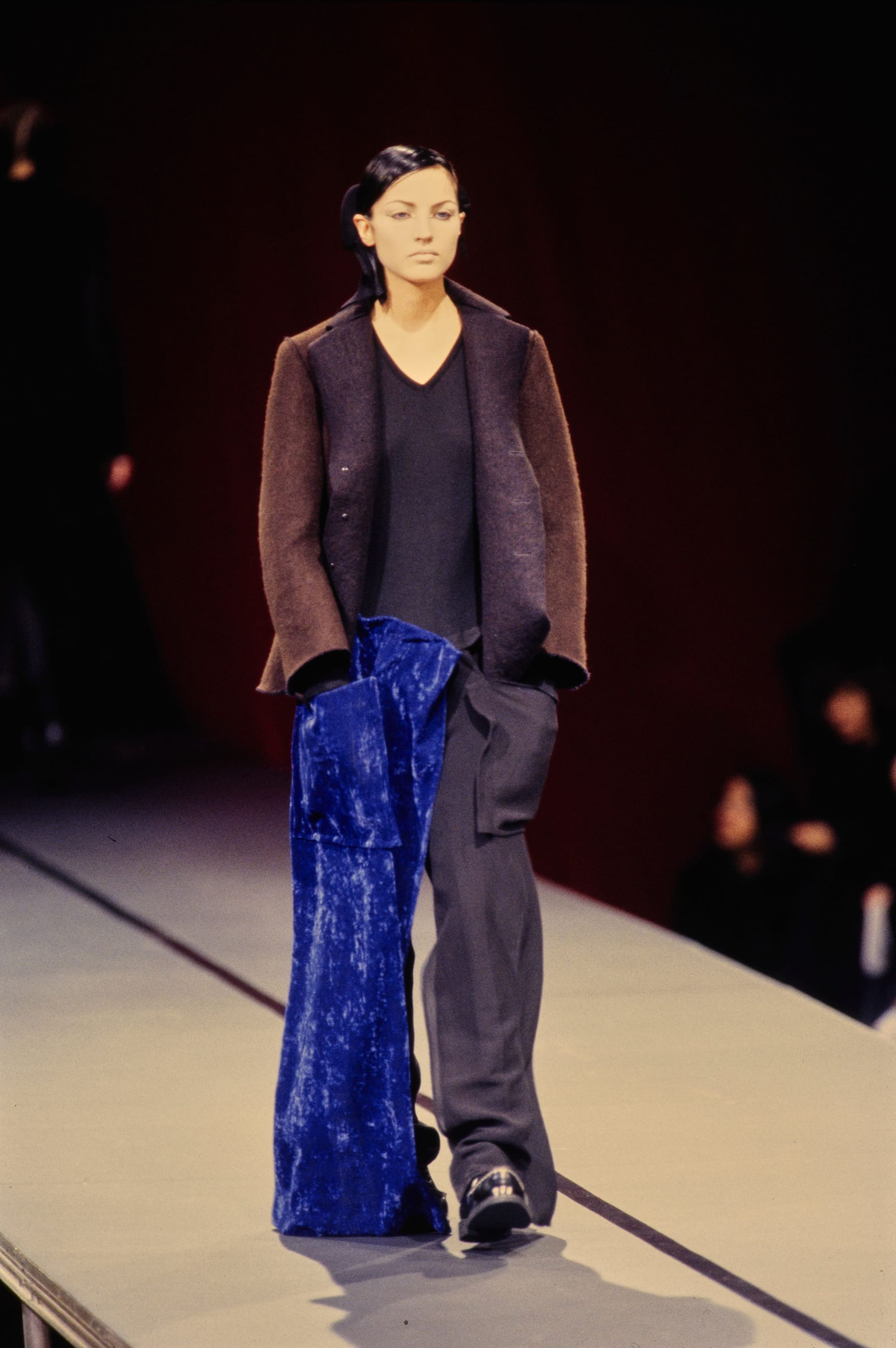 Yohji Yamamoto Fall 1995 detail 49: Brown jacket over a navy top and dark trousers with a long cobalt velvet panel.