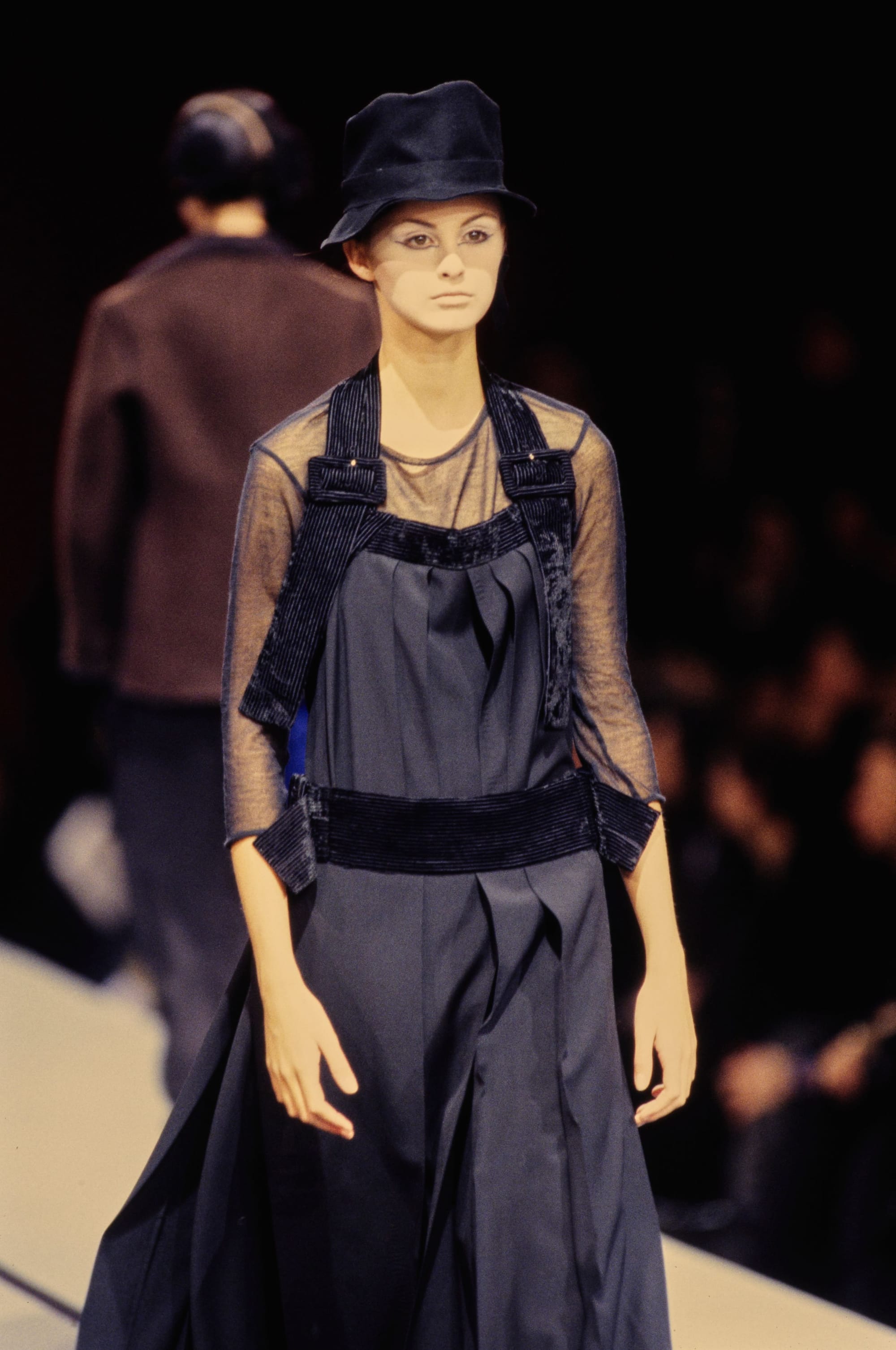 Yohji Yamamoto Fall 1995 detail 51: Black hat, sheer navy sleeves and a dark pinafore with broad shoulder and waist bands.