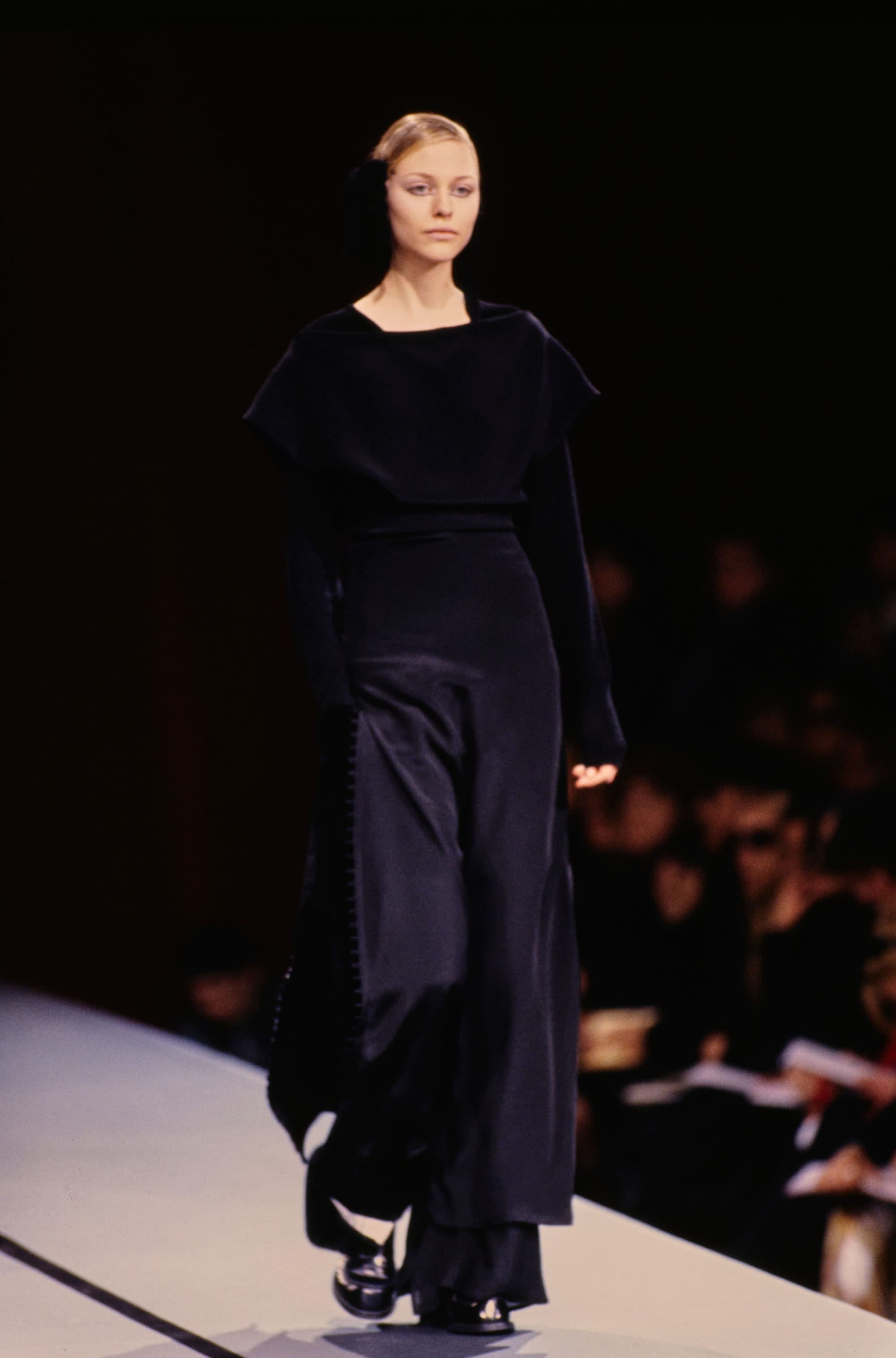 Yohji Yamamoto Fall 1995 detail 52: Long dark dress with a short cape-like shoulder layer and a defined waist.