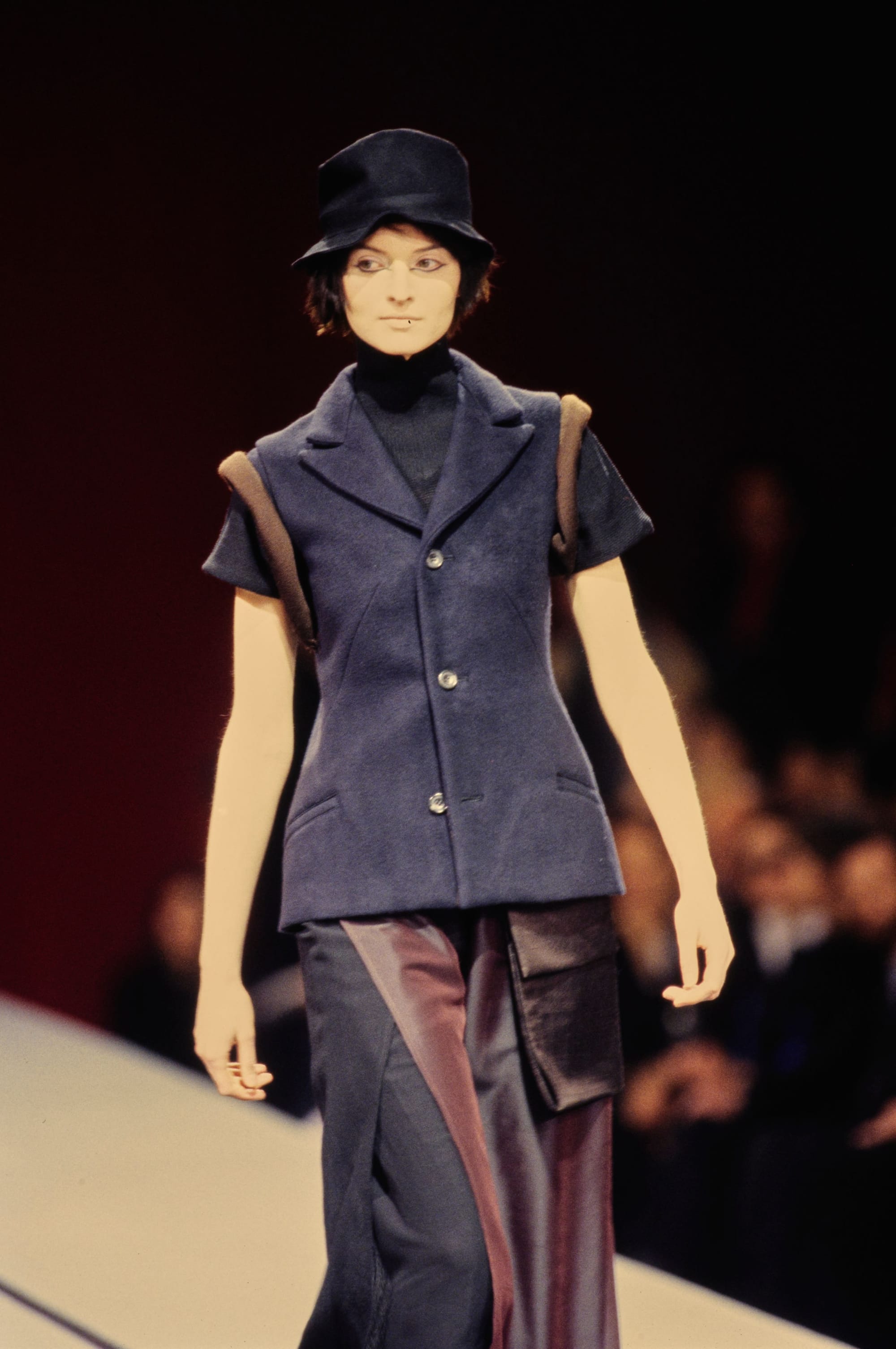 Yohji Yamamoto Fall 1995 detail 54: Black hat and short-sleeved navy tailored vest above two-tone wide trousers.