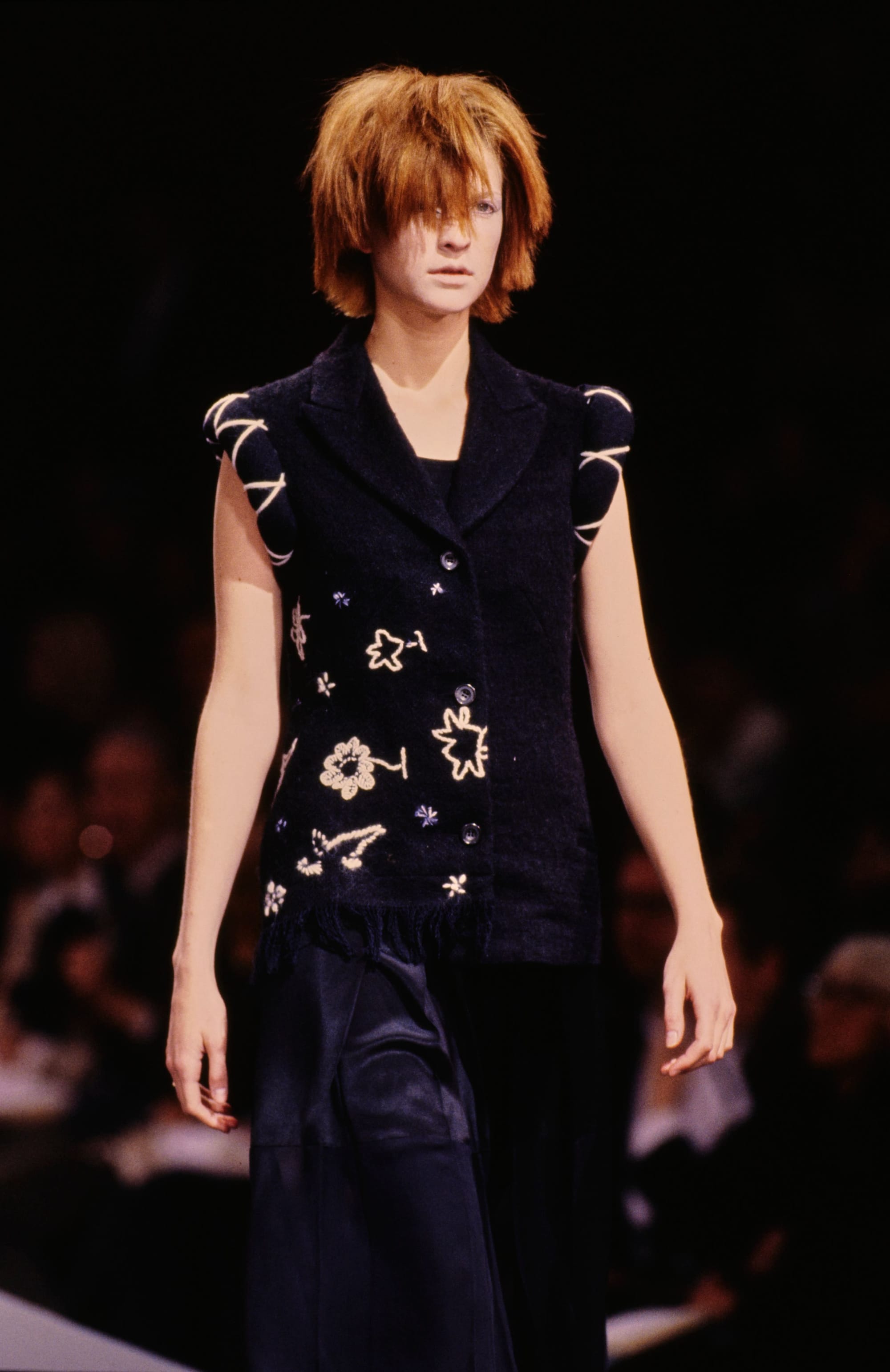 Yohji Yamamoto Fall 1995 detail 55: Sleeveless dark vest embroidered with small pale flowers above a layered navy skirt.