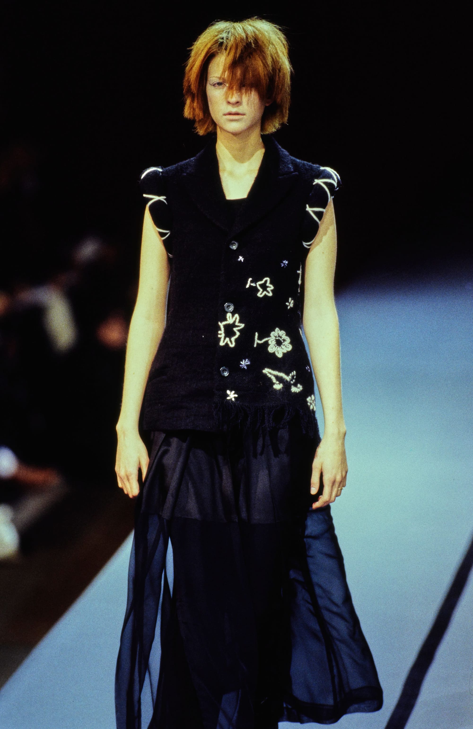 Yohji Yamamoto Fall 1995 detail 56: Full view of a black floral-embroidered sleeveless vest and flowing dark skirt.