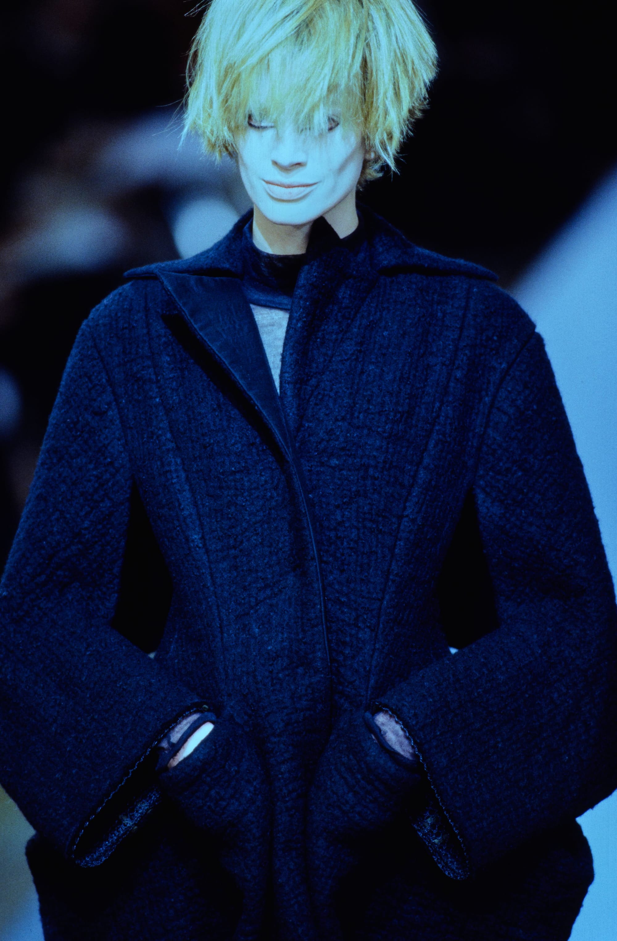 Yohji Yamamoto Fall 1995 detail 57: Close view of a textured navy coat with angular lapels and openings by the hands.