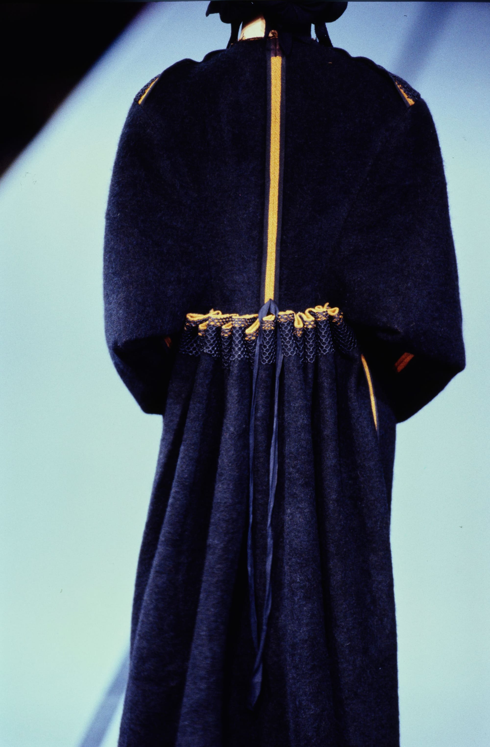 Yohji Yamamoto Fall 1995 detail 62: Rear close view of a navy coat with a mustard center stripe and gathered waist.